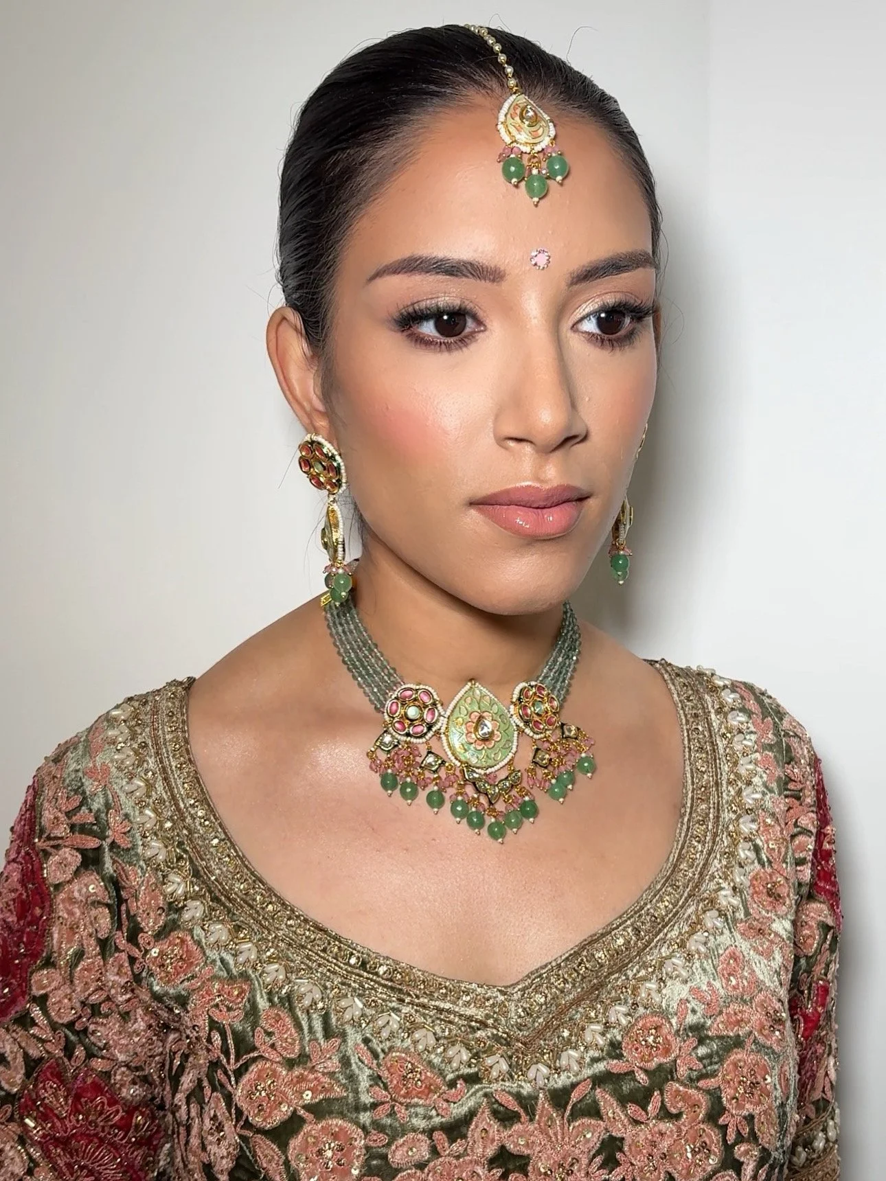 Woman wearing traditional Indian jewelry and a richly embroidered blouse.
