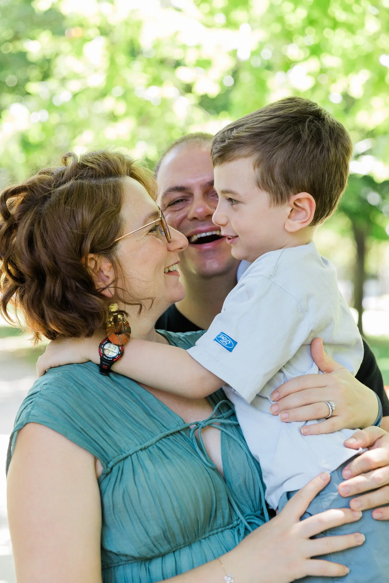 A cheerful family moment with a woman holding a smiling young boy in a park setting.