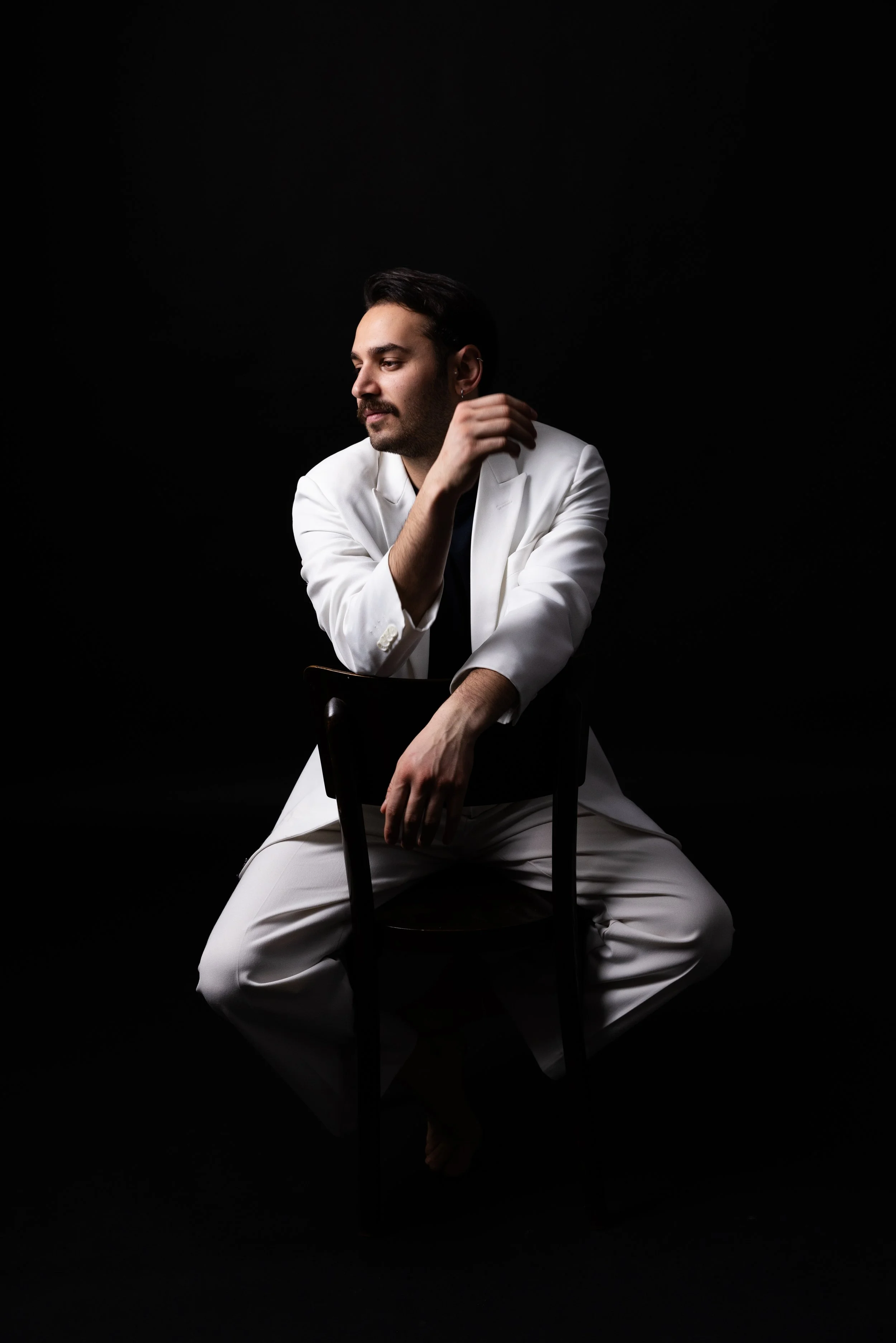 Man in white suit posing on chair against black background