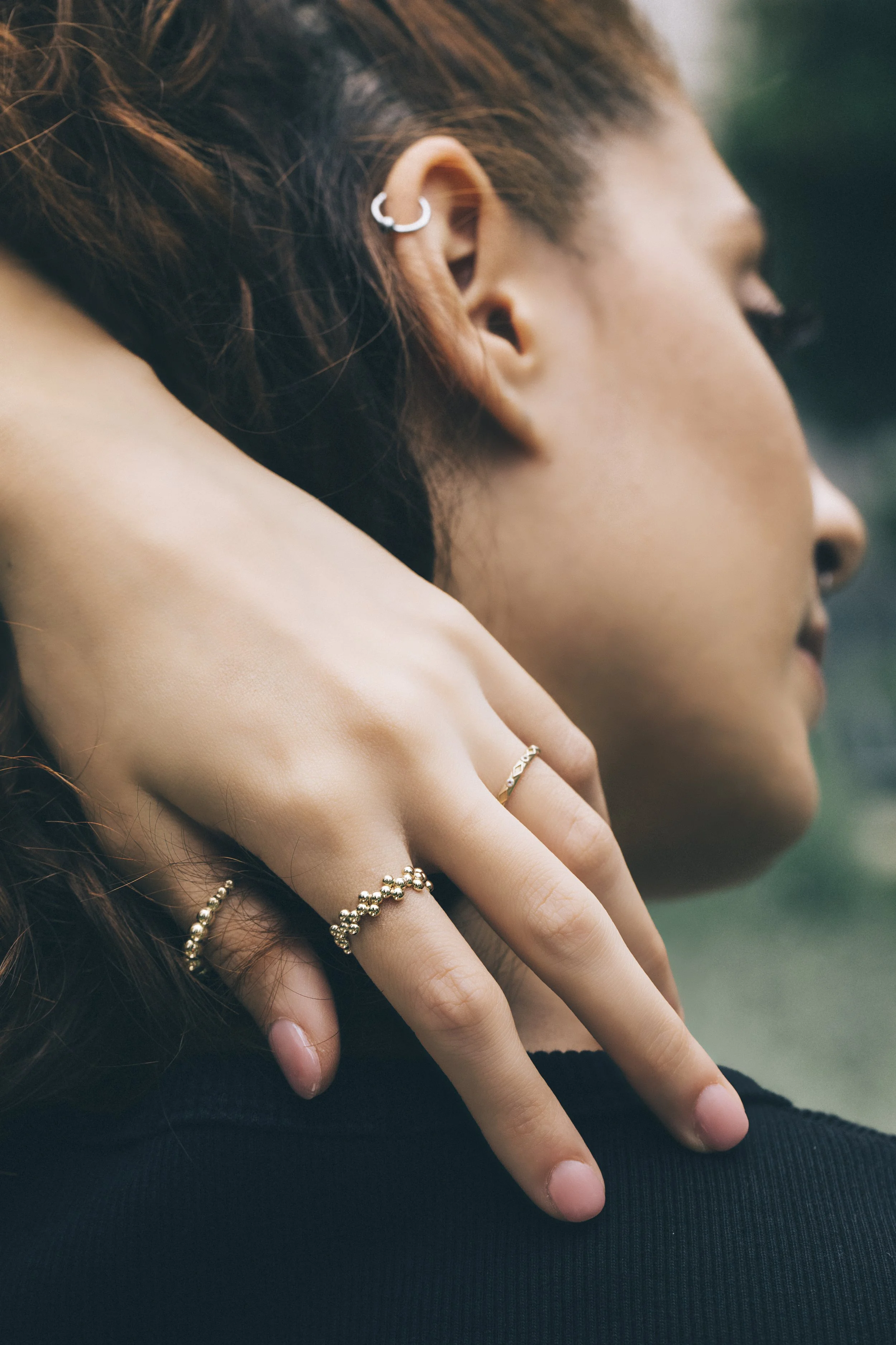 Close-up of a person wearing gold rings on fingers, showing an ear cuff on the ear.