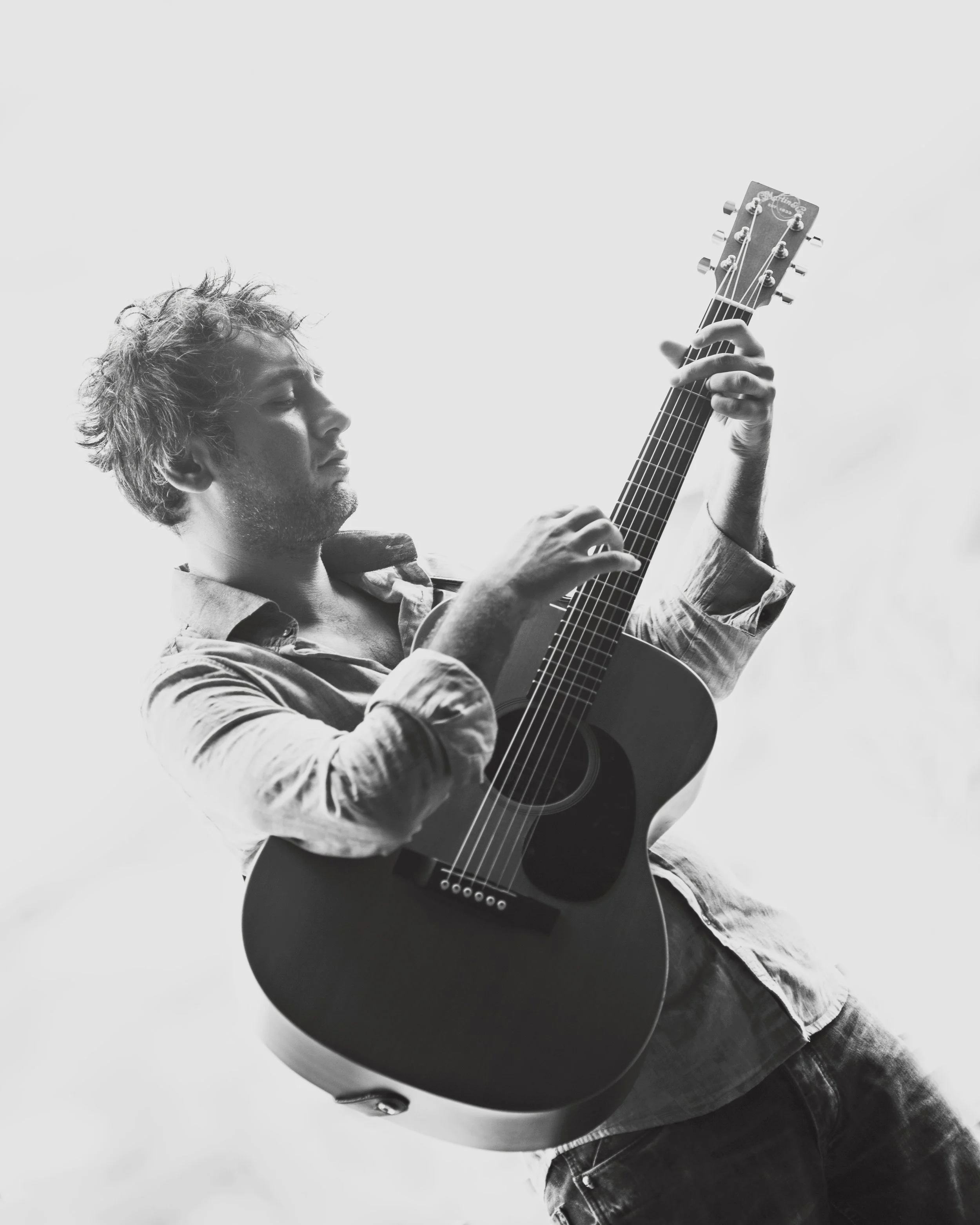 Black and white photo of a person playing an acoustic guitar, wearing a casual shirt.