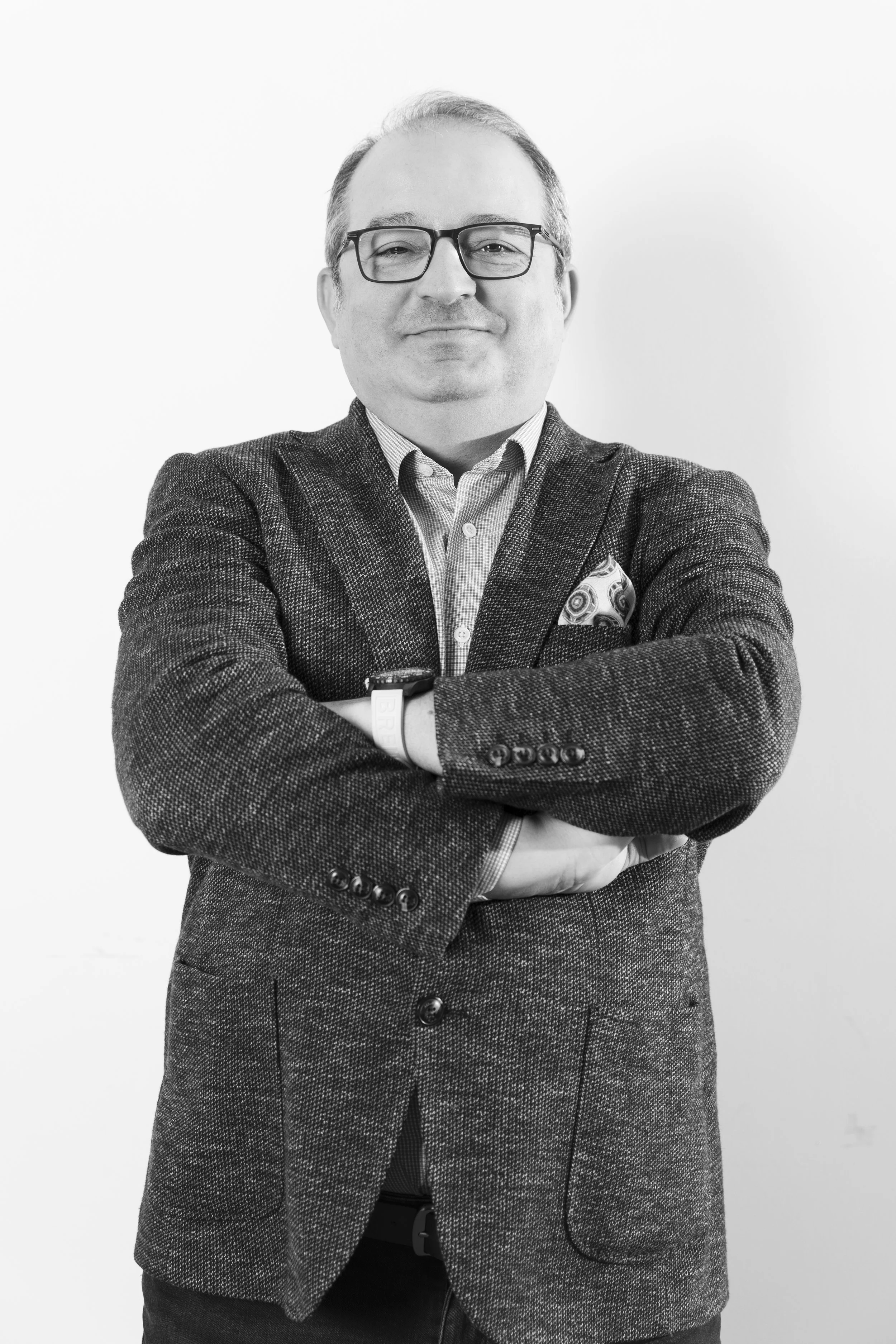 Confident man in glasses and blazer with arms crossed against white background.