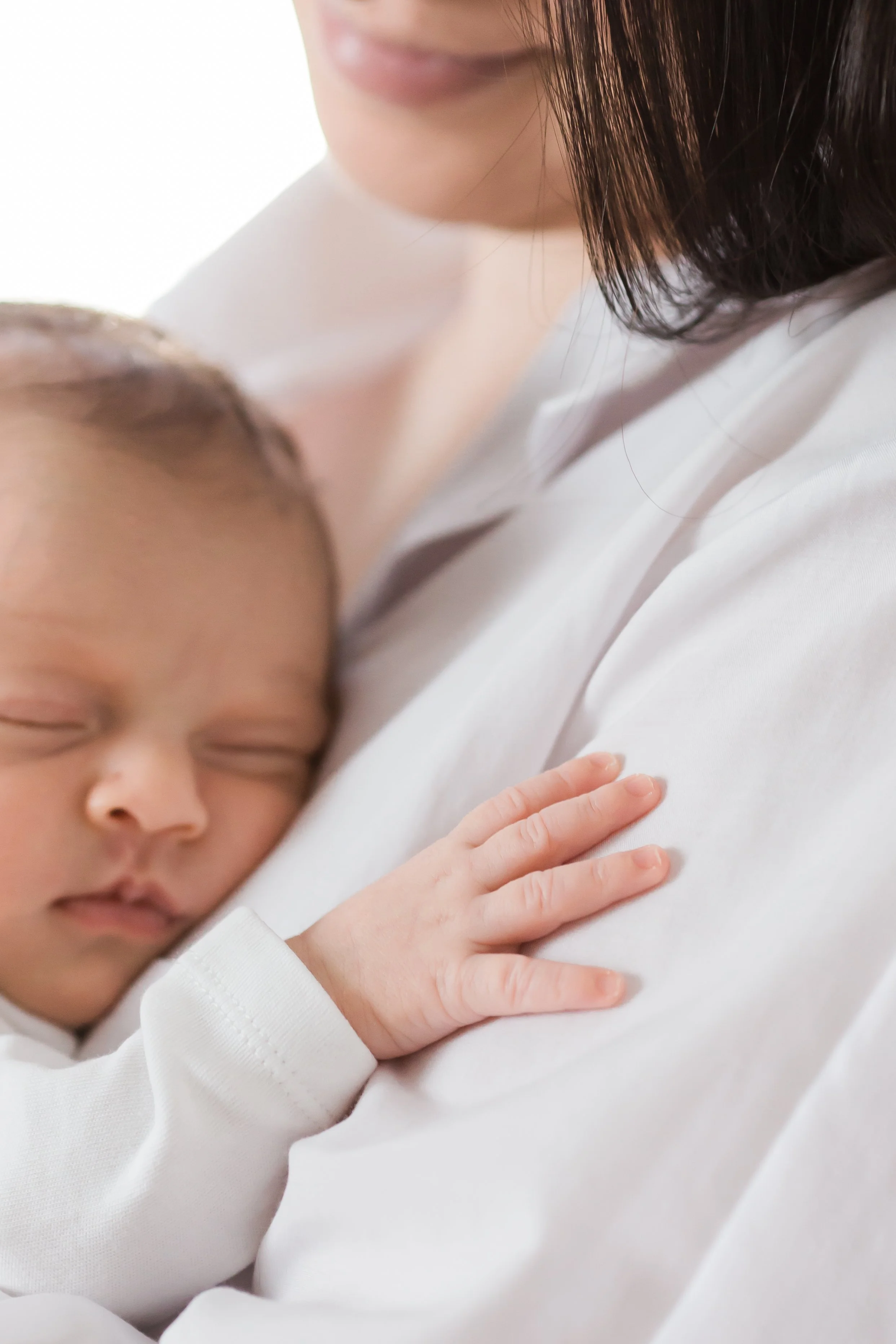 A sleeping baby in a white outfit resting on a person's shoulder.