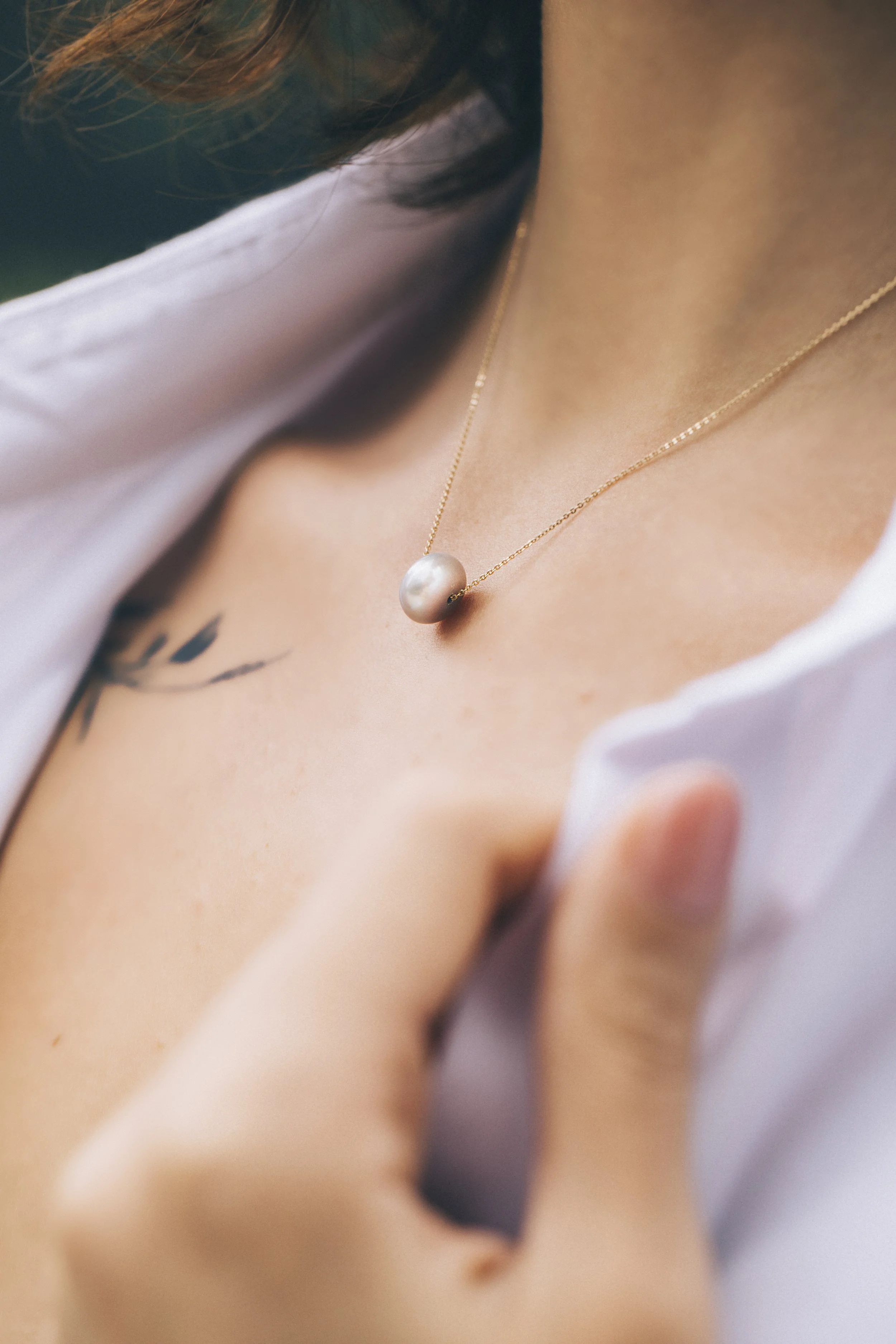 Close-up of a pearl necklace on a woman's neck with a tattoo and a partially visible white shirt.