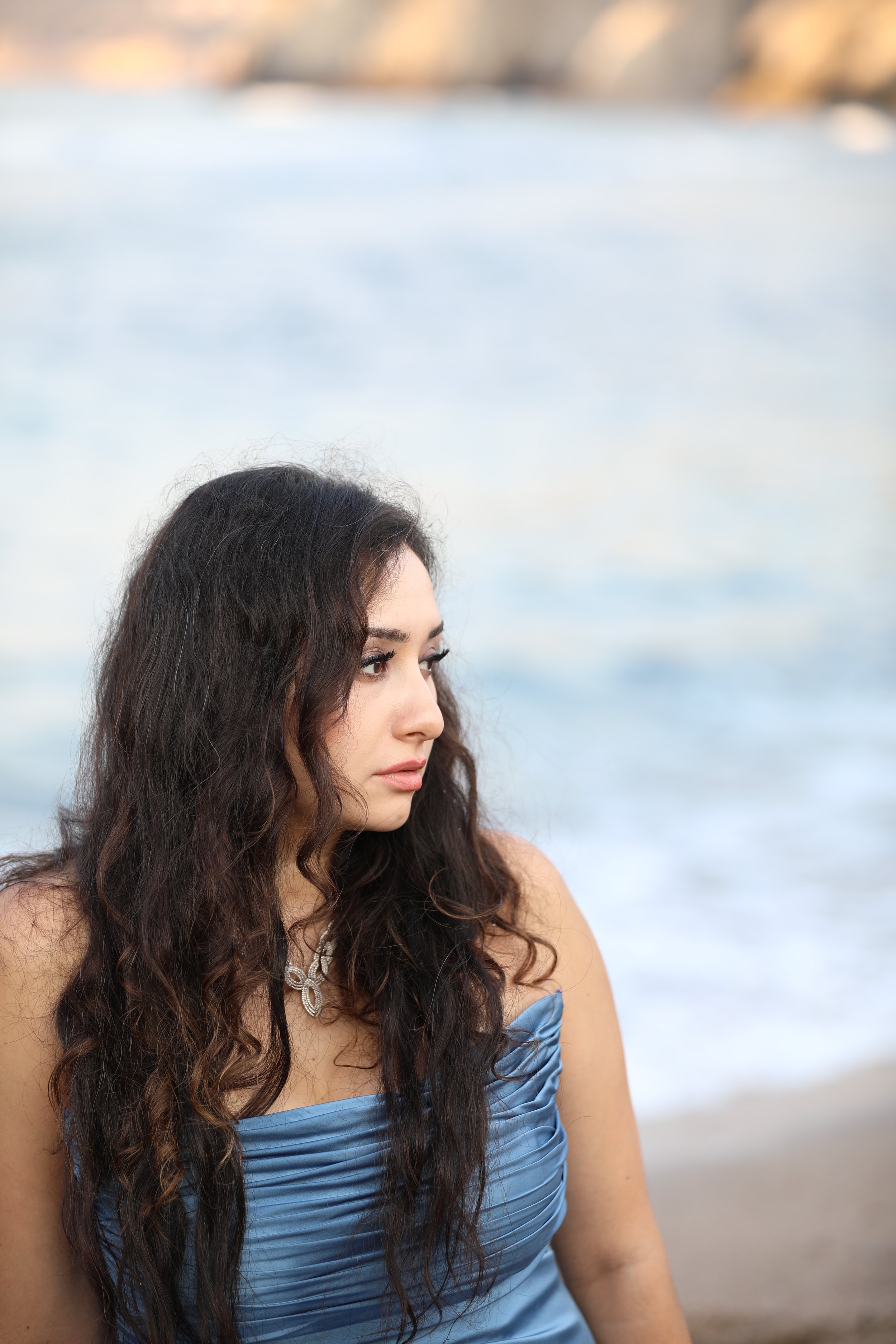 Woman with long curly hair in a blue dress sitting on a beach