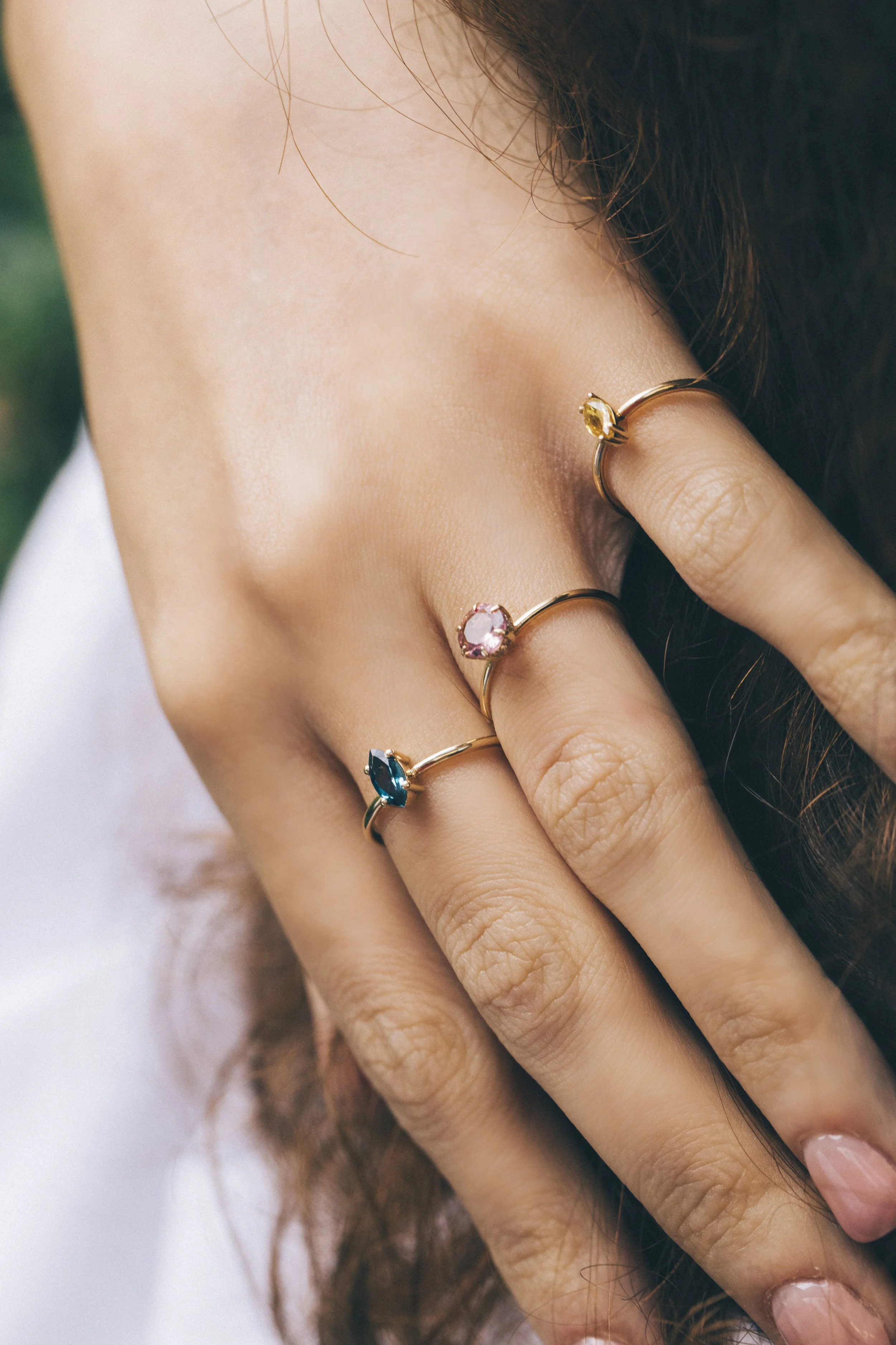 Hand with three rings featuring pink, blue, and yellow gemstones.