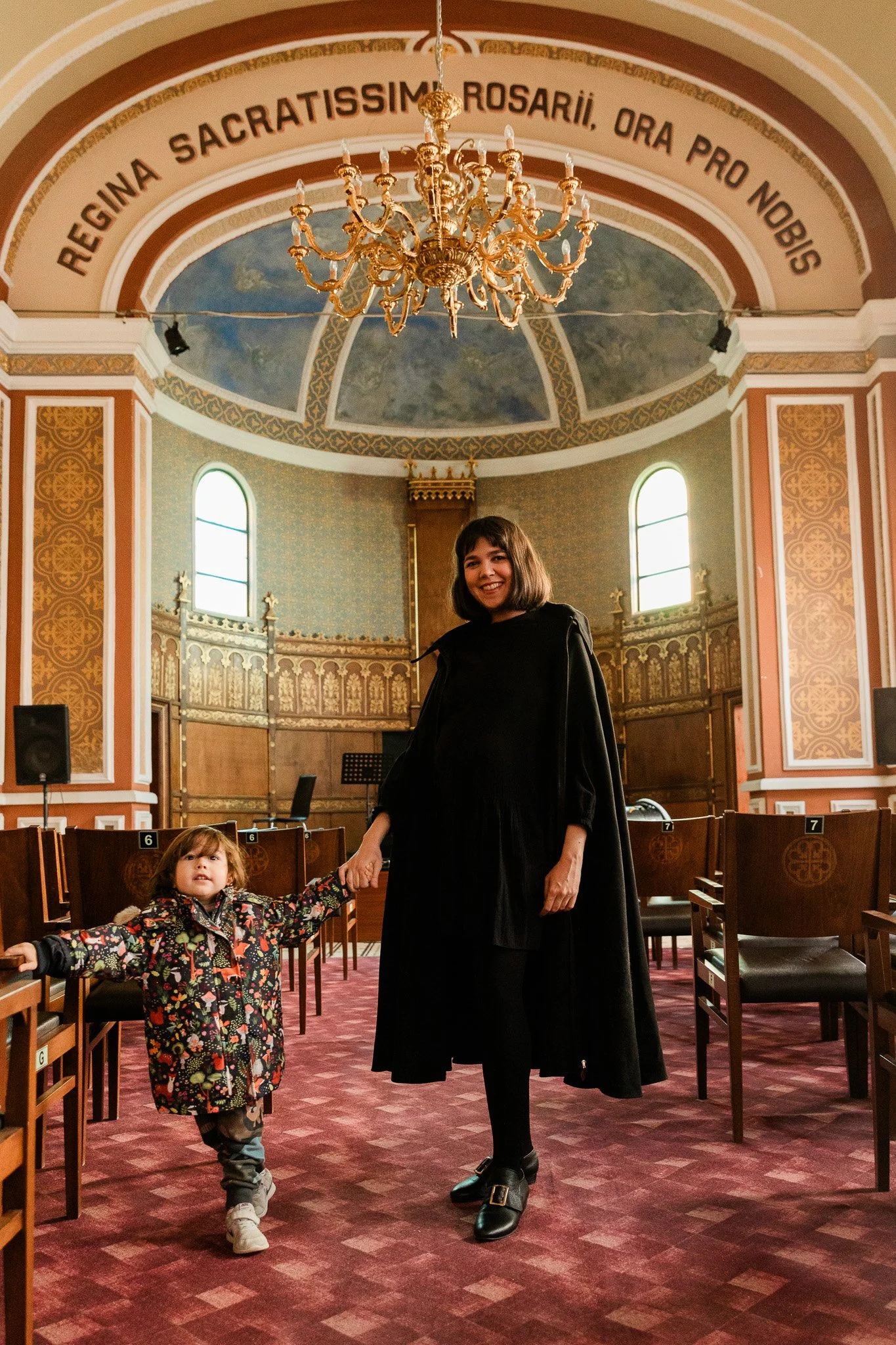 Woman and child inside a church with ornate decoration and chandelier.