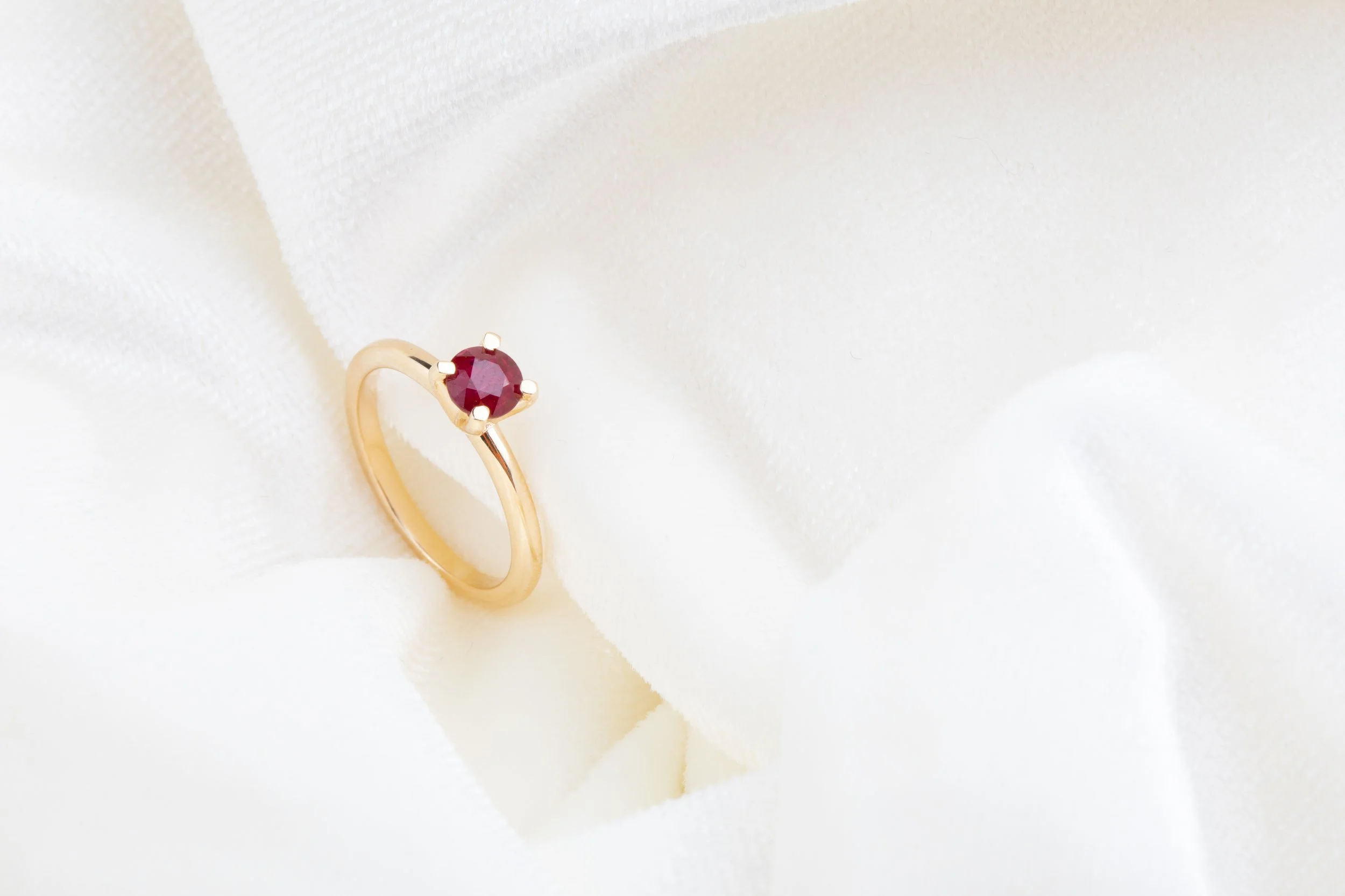 Gold ring with a red gemstone on white fabric