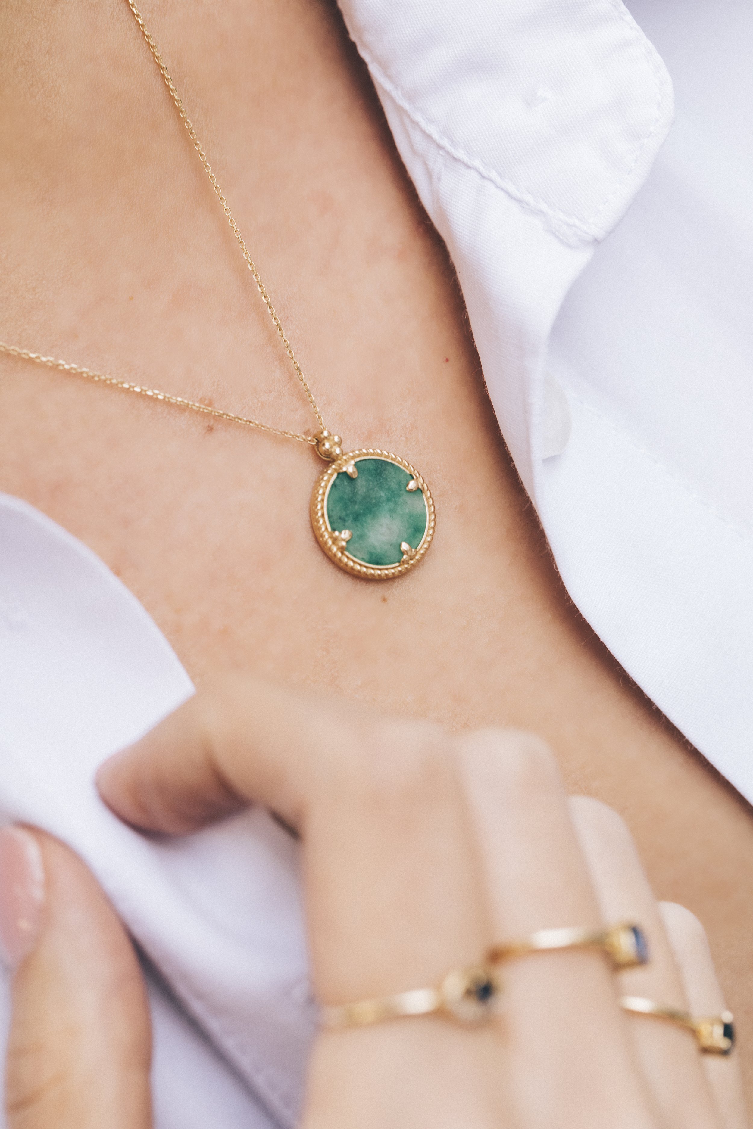 Gold necklace with green stone pendant on person wearing a white shirt.