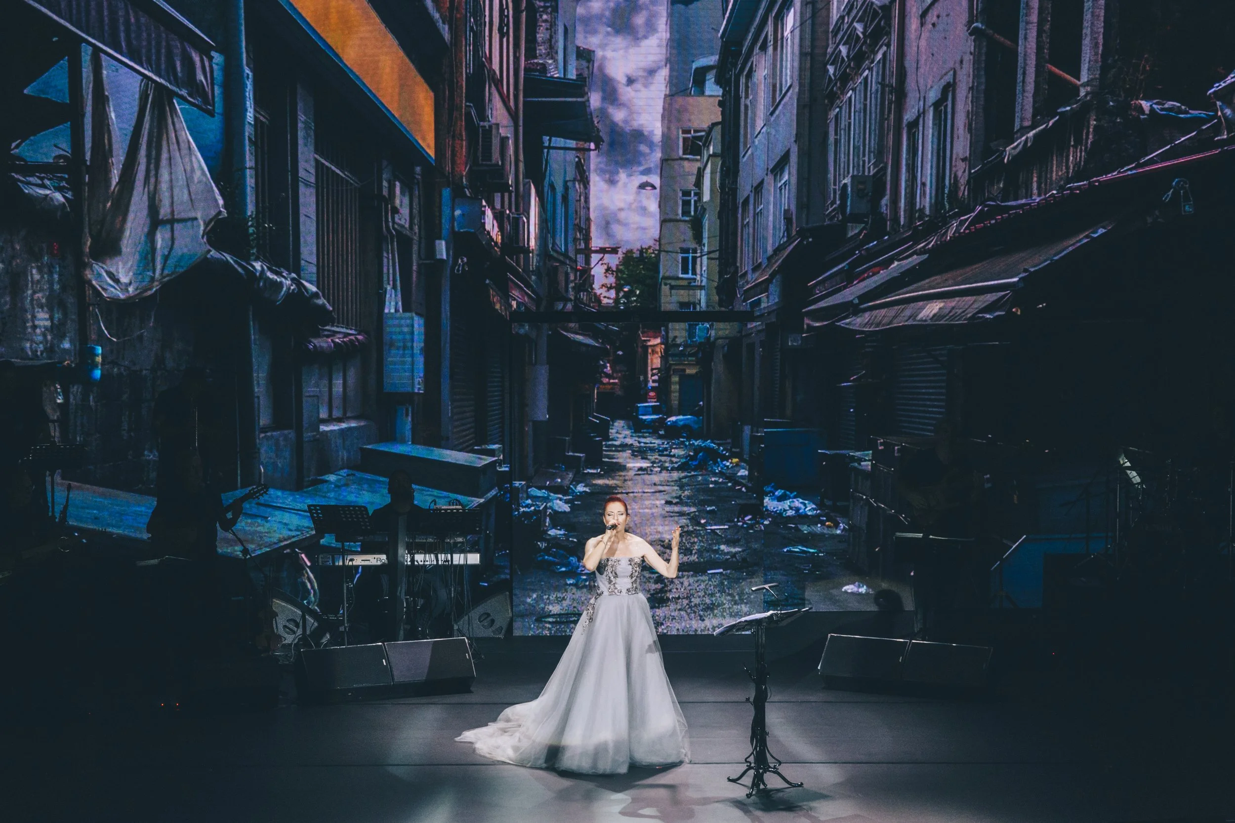 Singer performing on a stage with a gritty urban alleyway background.