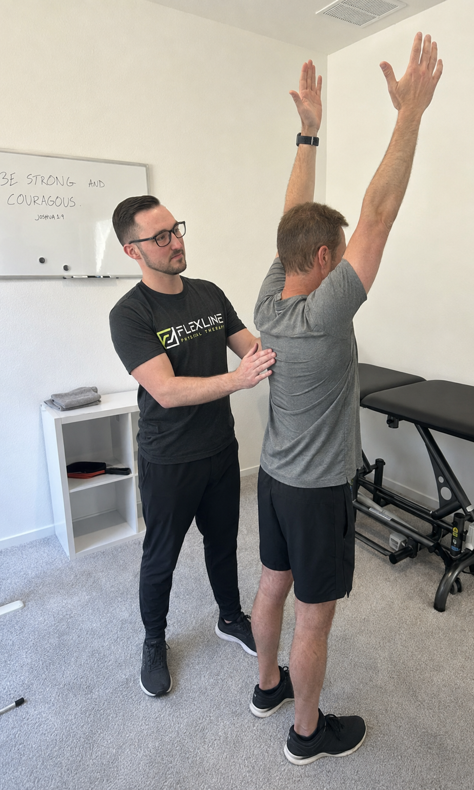 Physical therapist assessing overhead shoulder mobility to find the cause of pain when reaching above the head