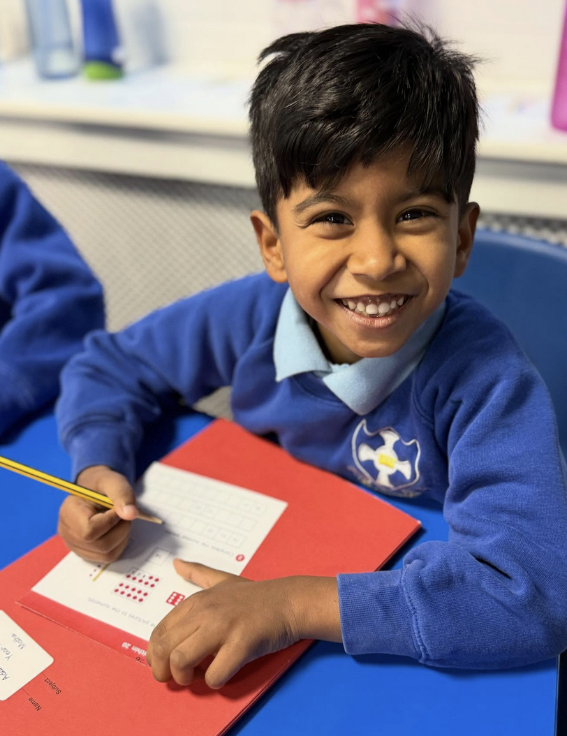 Smiling elementary school boy in blue uniform writing in a workbook at a classroom desk