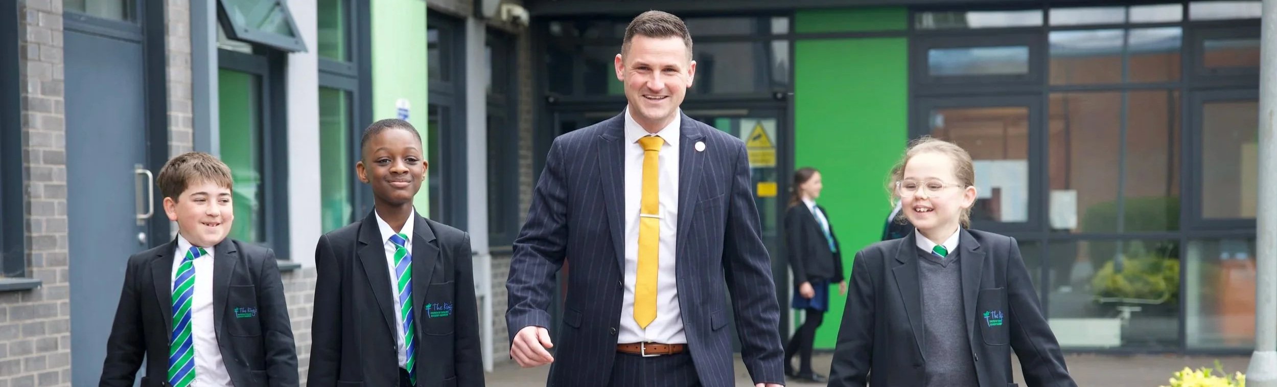 School principal walking with three uniformed students outside a school building