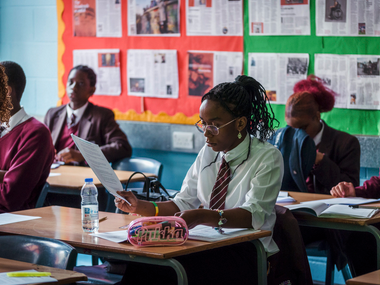 High school students in uniforms studying at desks in a classroom with newspaper displays