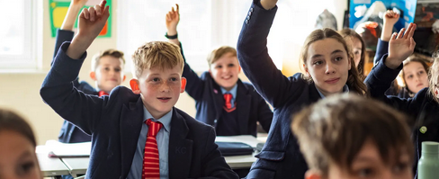 Schoolchildren in uniforms raising their hands during a classroom lesson