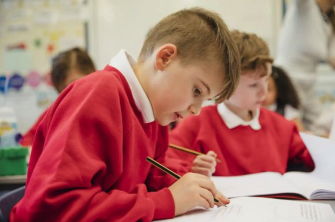 Schoolchildren in red uniforms writing in notebooks at a classroom desk