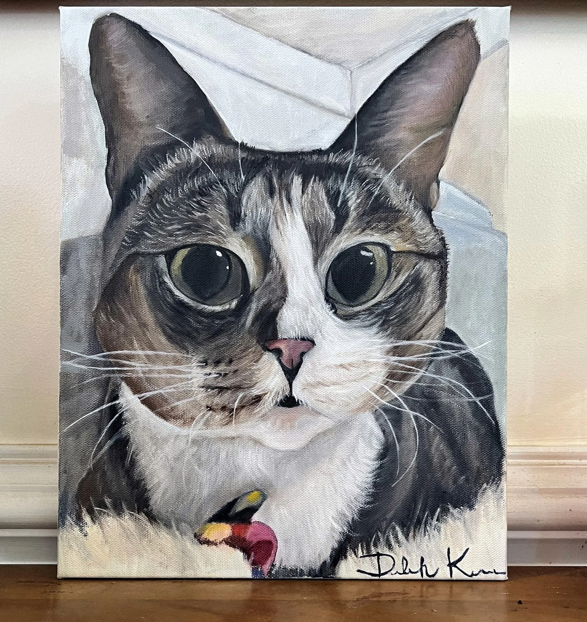 A detailed painting of a tabby cat with large, expressive eyes, a pink nose, and white and brown fur. The artist's signature "Debi K" is in the bottom right corner.