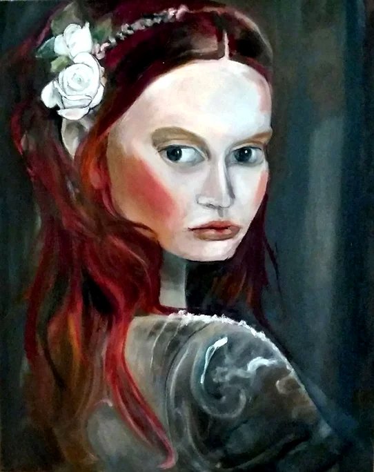 A woman with long red hair, decorated with white flowers, taking a selfie. She has fair skin, red makeup, and is wearing a dark top.