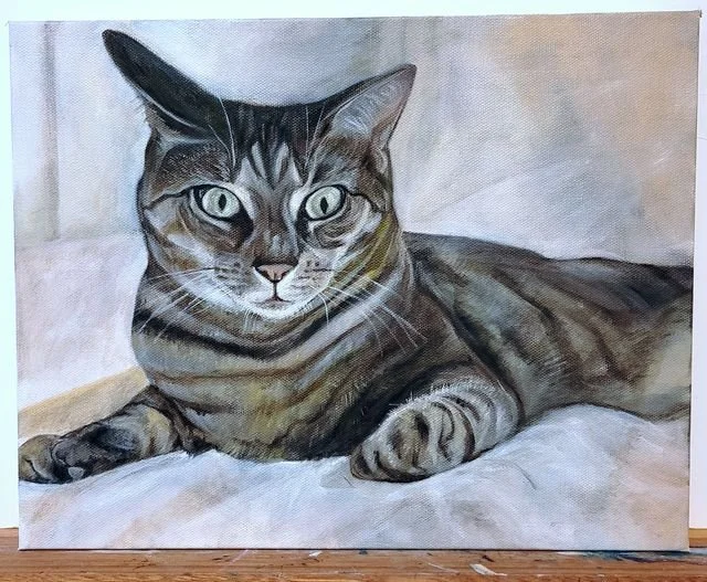 A detailed painting of a tabby cat lying on a bed, with green eyes and striped fur, facing forward.