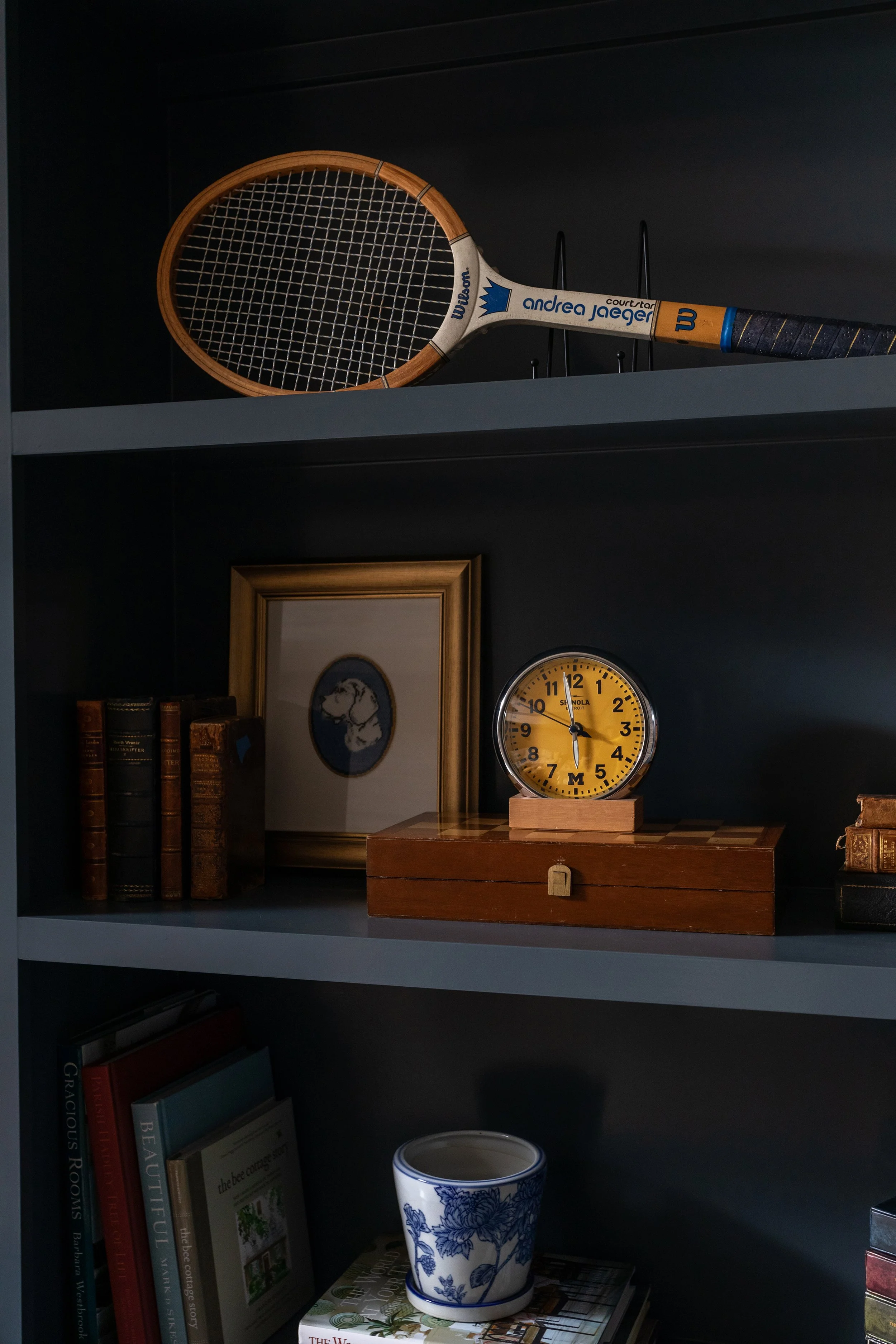 Custom dark blue built-in shelving displaying a vintage tennis racket, books, artwork, and collected pieces.