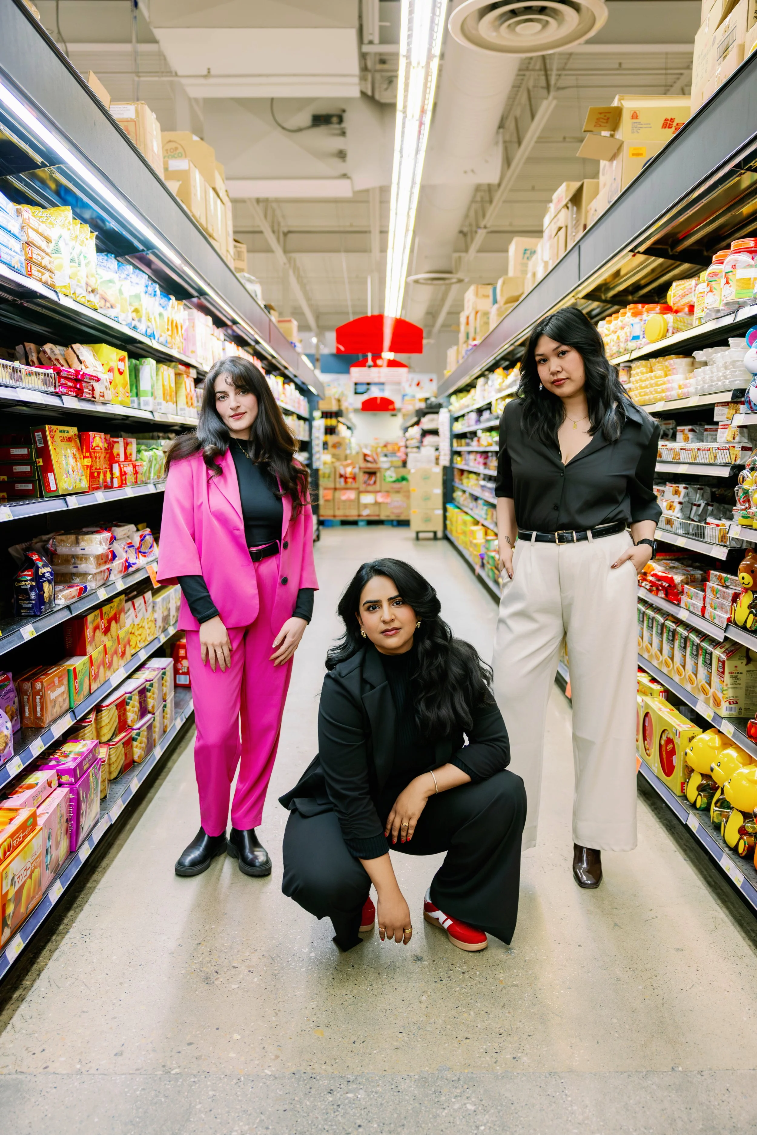 Four women in fashionable clothing posing in the snack aisle of a grocery store facing the camera.