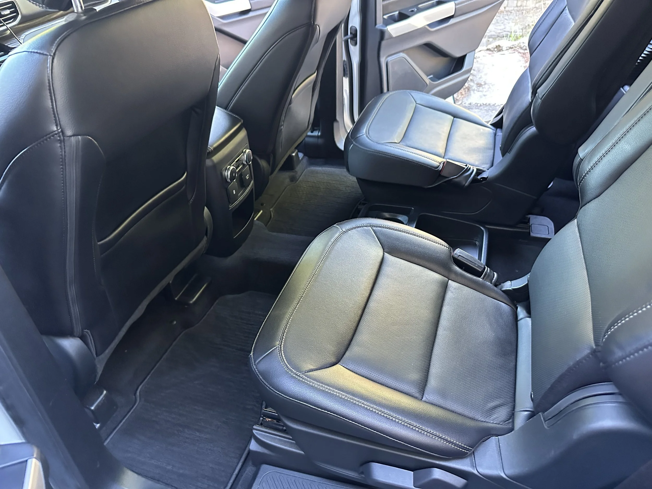The back seats of a vehicle with black leather upholstery, showing the front of the second row and part of the third row with fold-up seats.