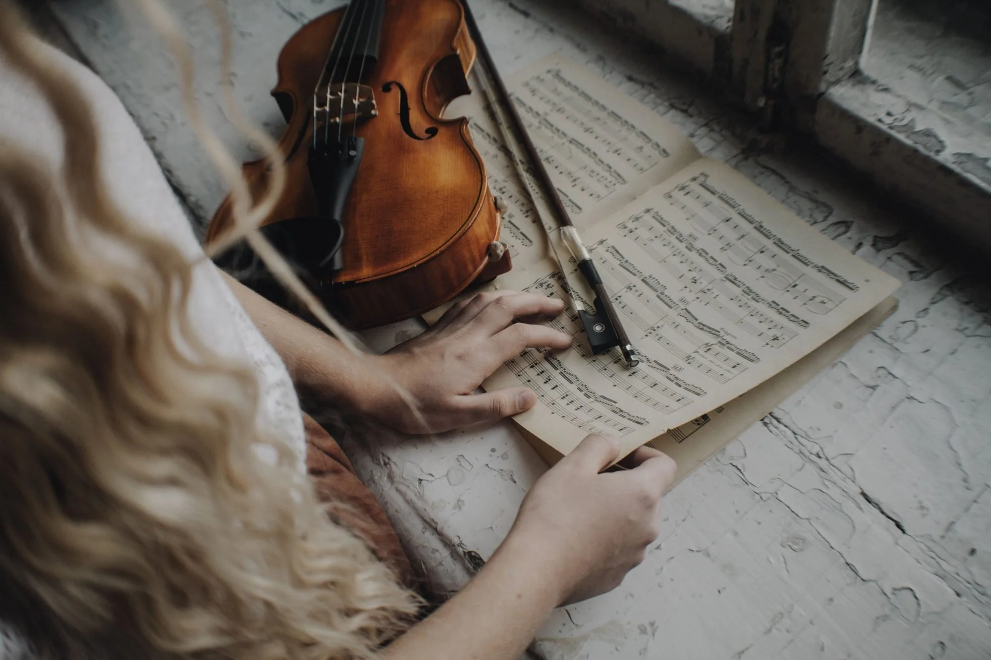 Violin and bow resting on sheet music beside a window