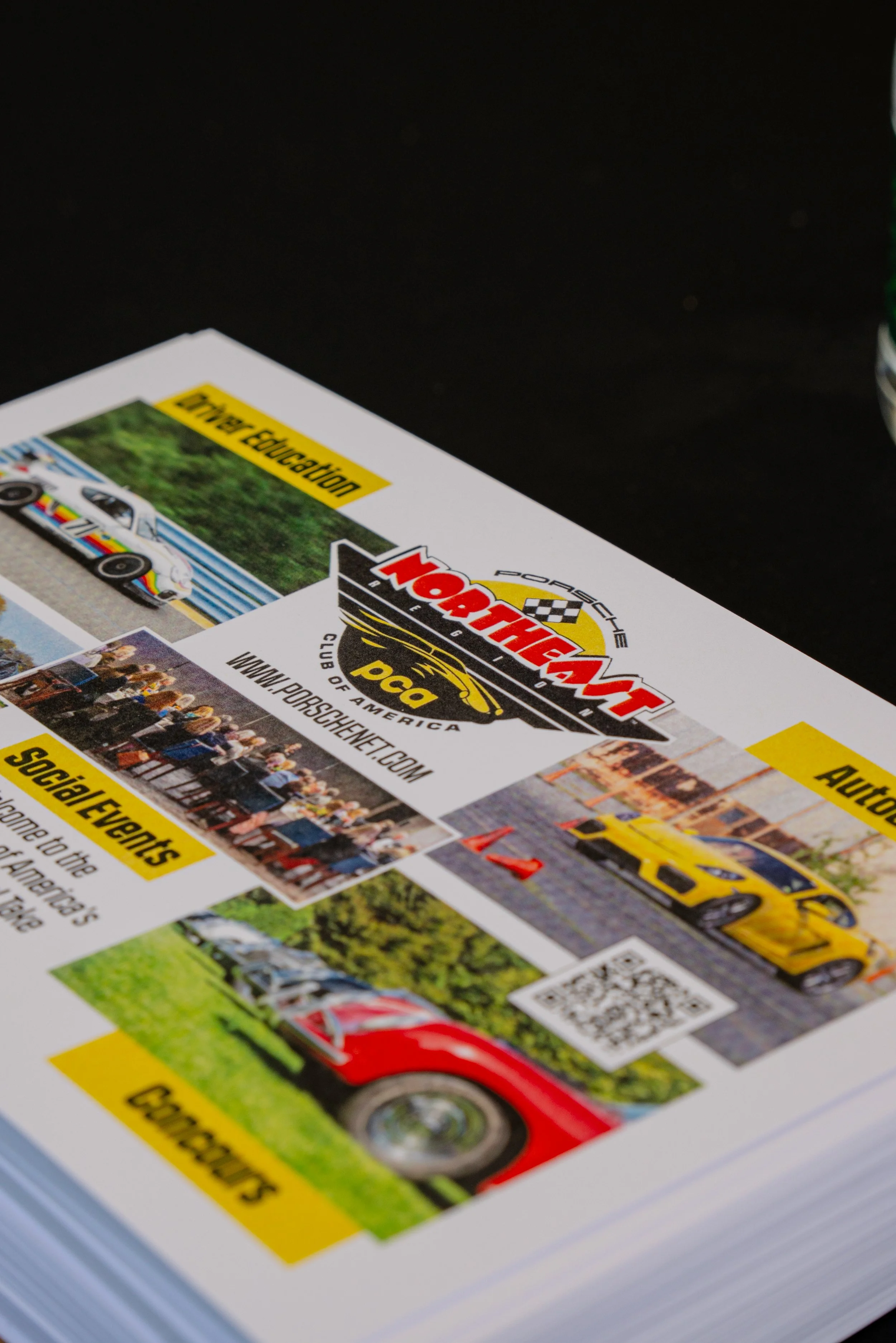 A close-up of a printed flyer for Porsche North America, featuring images of cars, social events, and text about automotive education and club activities.