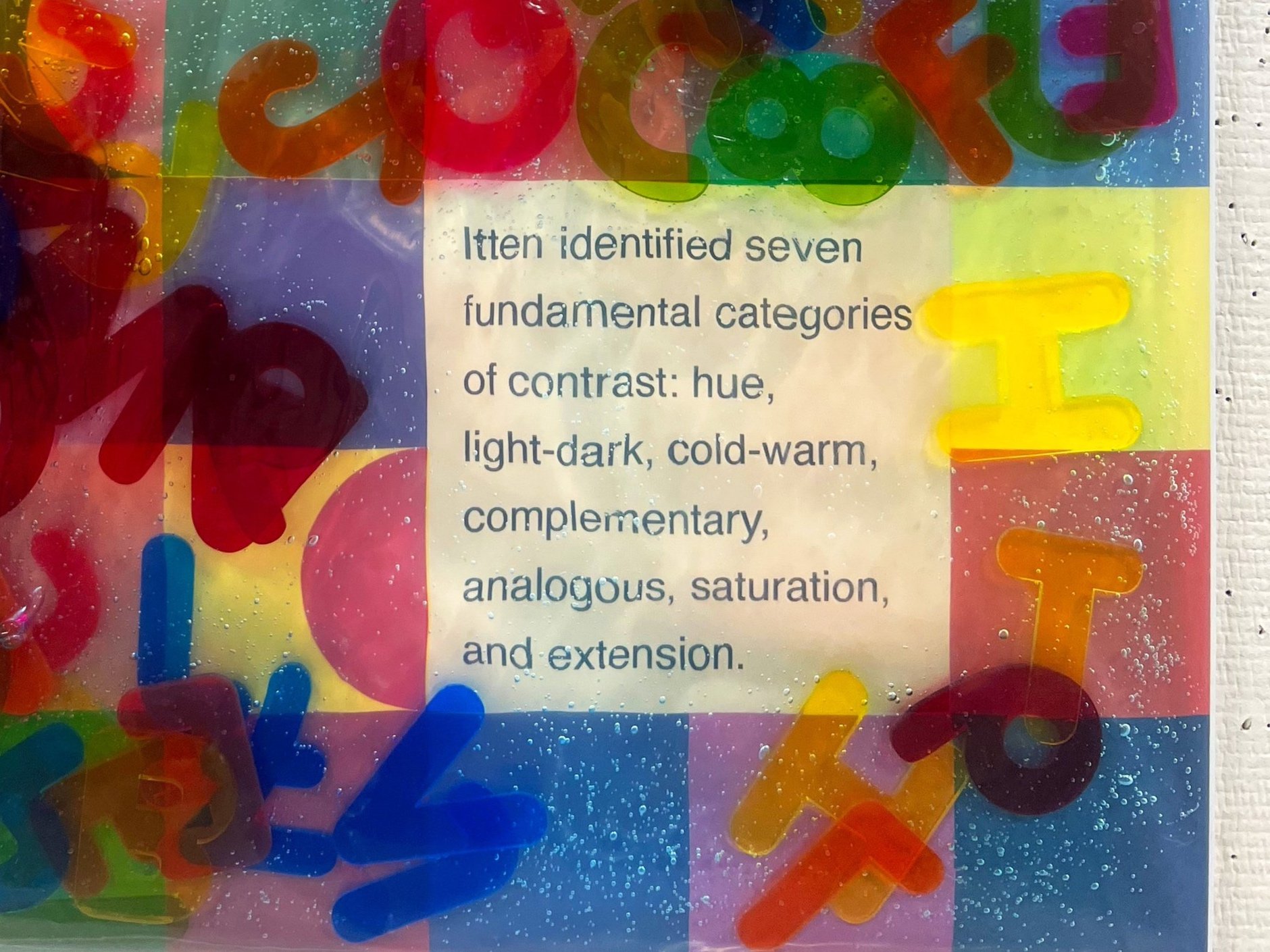 Colorful word magnets surrounding a card with text about seven fundamental color categories, including hue, light-dark, cold-warm, complementary, analogous, saturation, and extension.