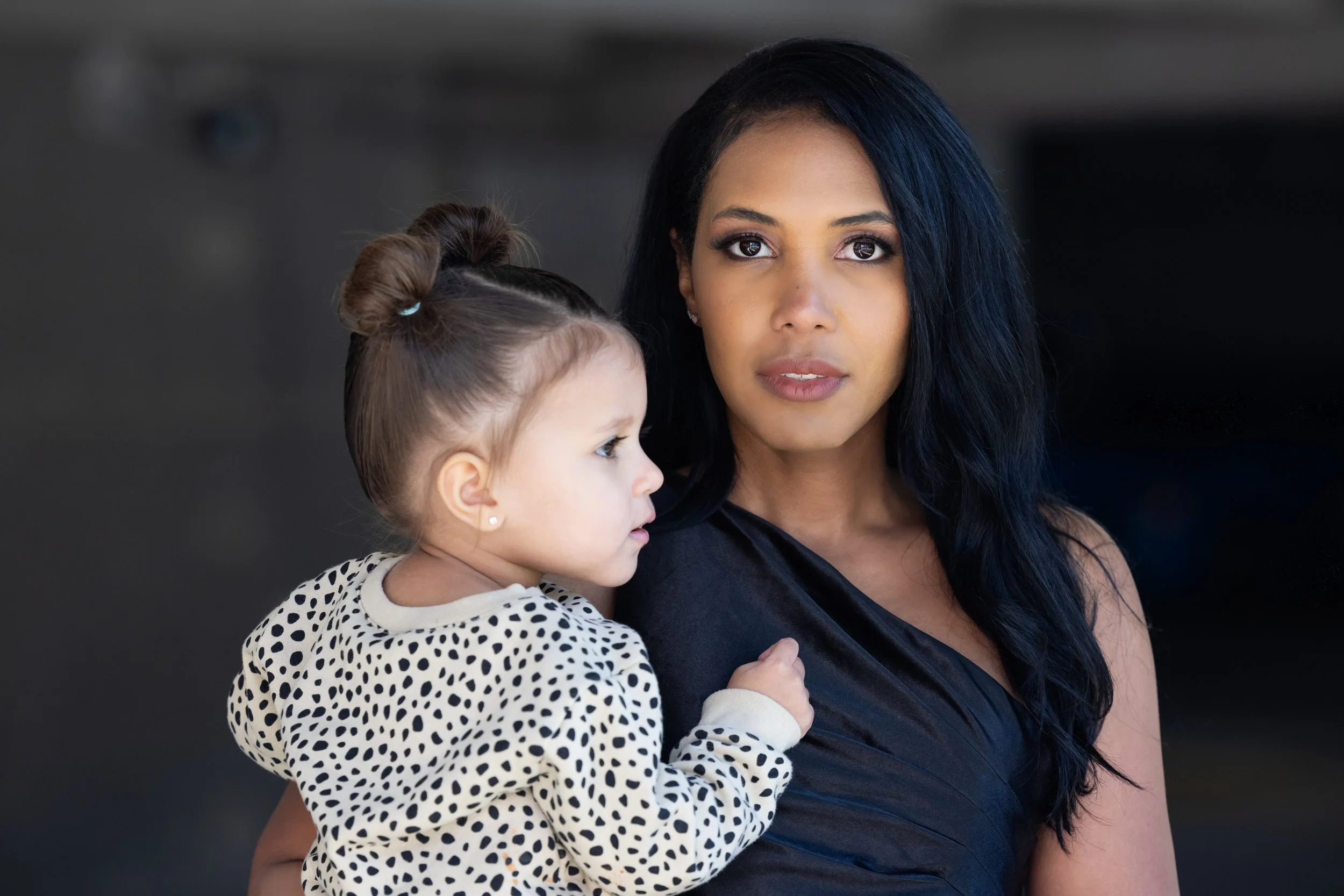 Woman holding a young child, both with serious expressions, against a blurred background.
