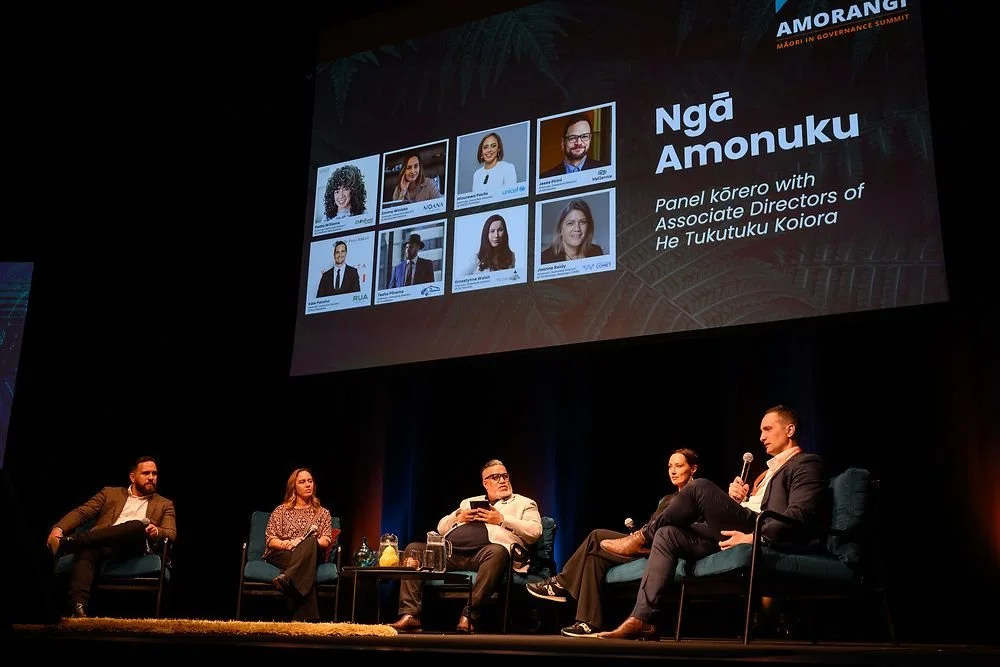 Panel discussion at an event with a large screen displaying headshots of panelists and the name Ngā Amonuku