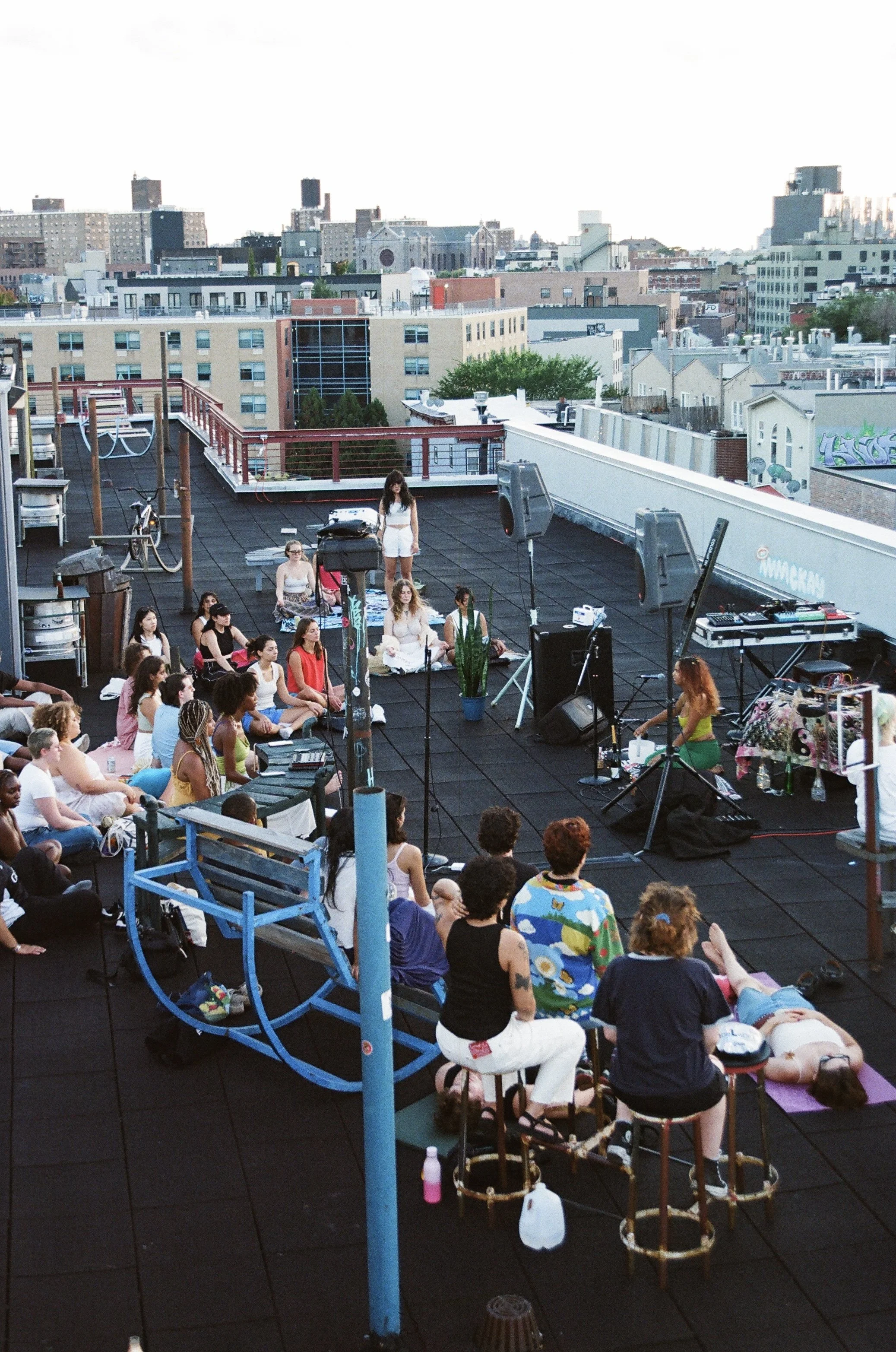 People attending a rooftop yoga or meditation class at sunset, with city buildings in the background.