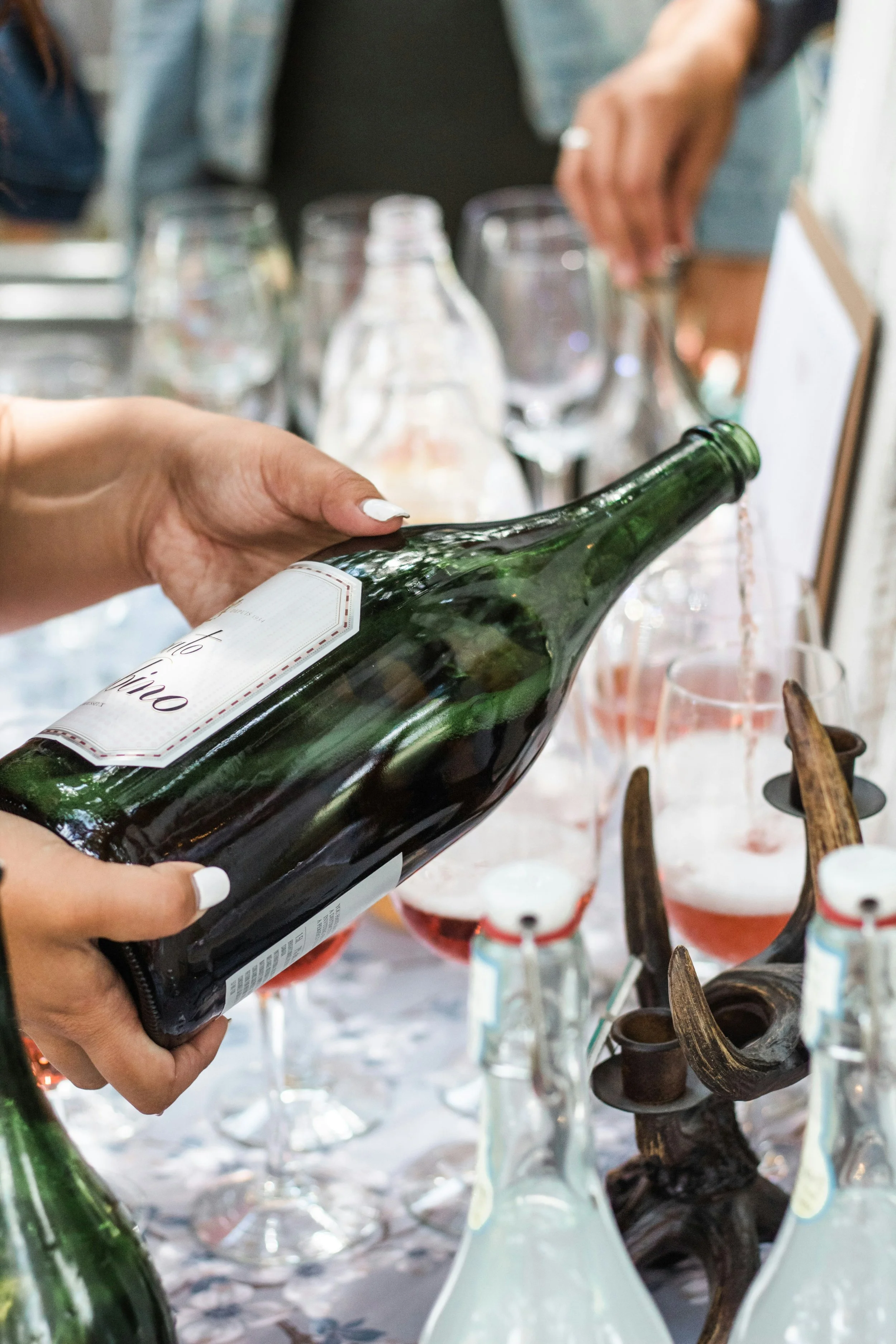 Person pouring pink wine into glasses at a table decorated with antlers and bottles.