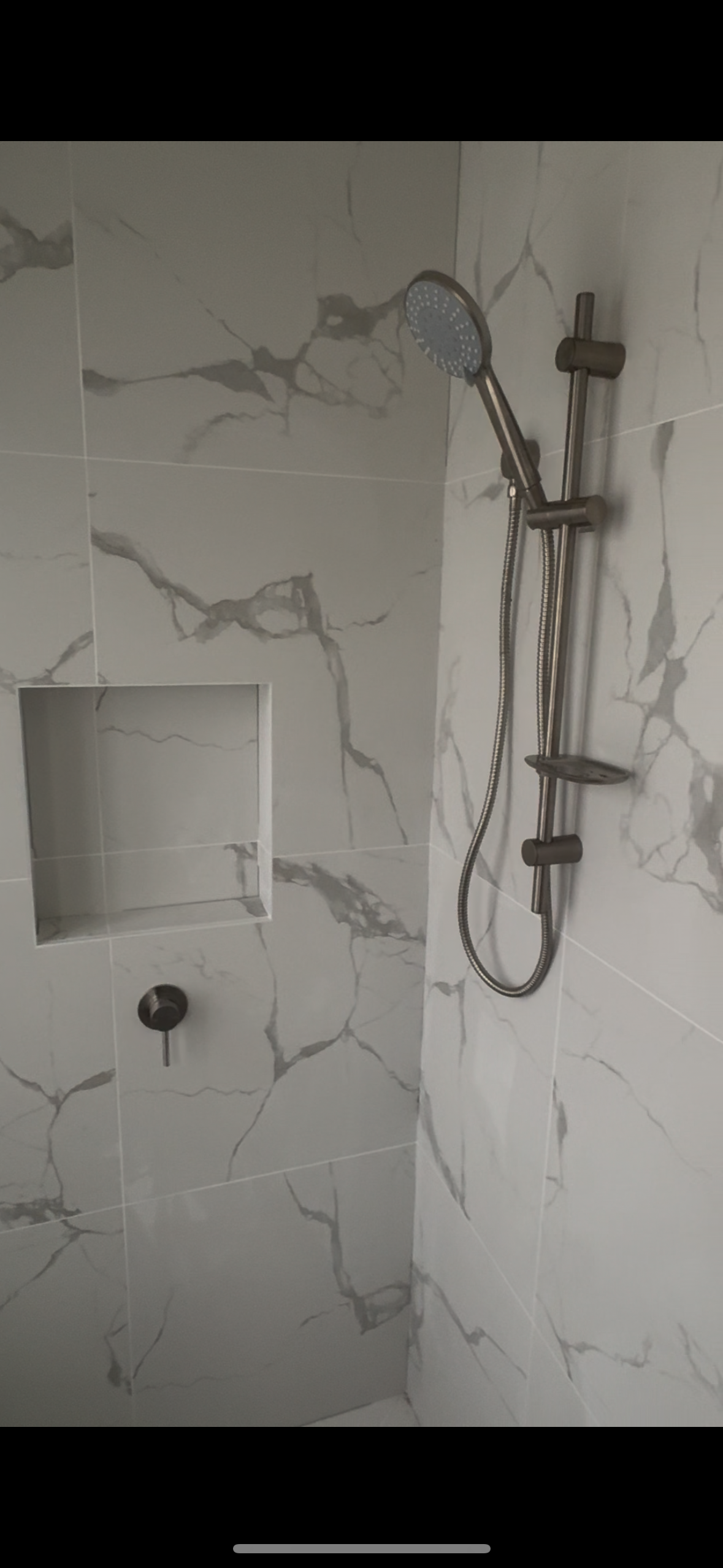 Marble tiled shower with a built-in niche, a handheld showerhead, and a soap shelf.