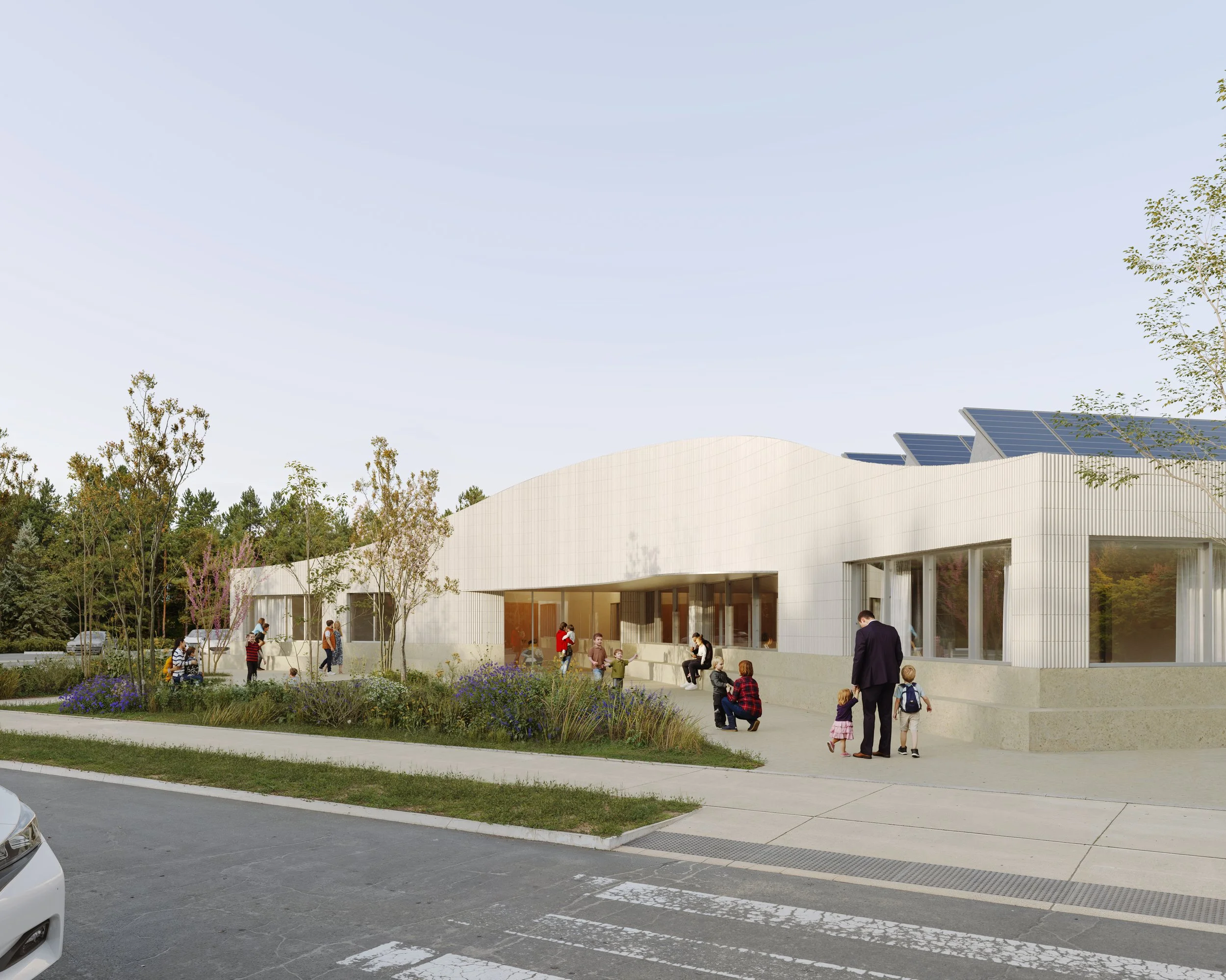 Modern school building with solar panels on the roof, surrounded by trees and greenery. Children and adults are seen outside, with some talking and others walking on the sidewalk.