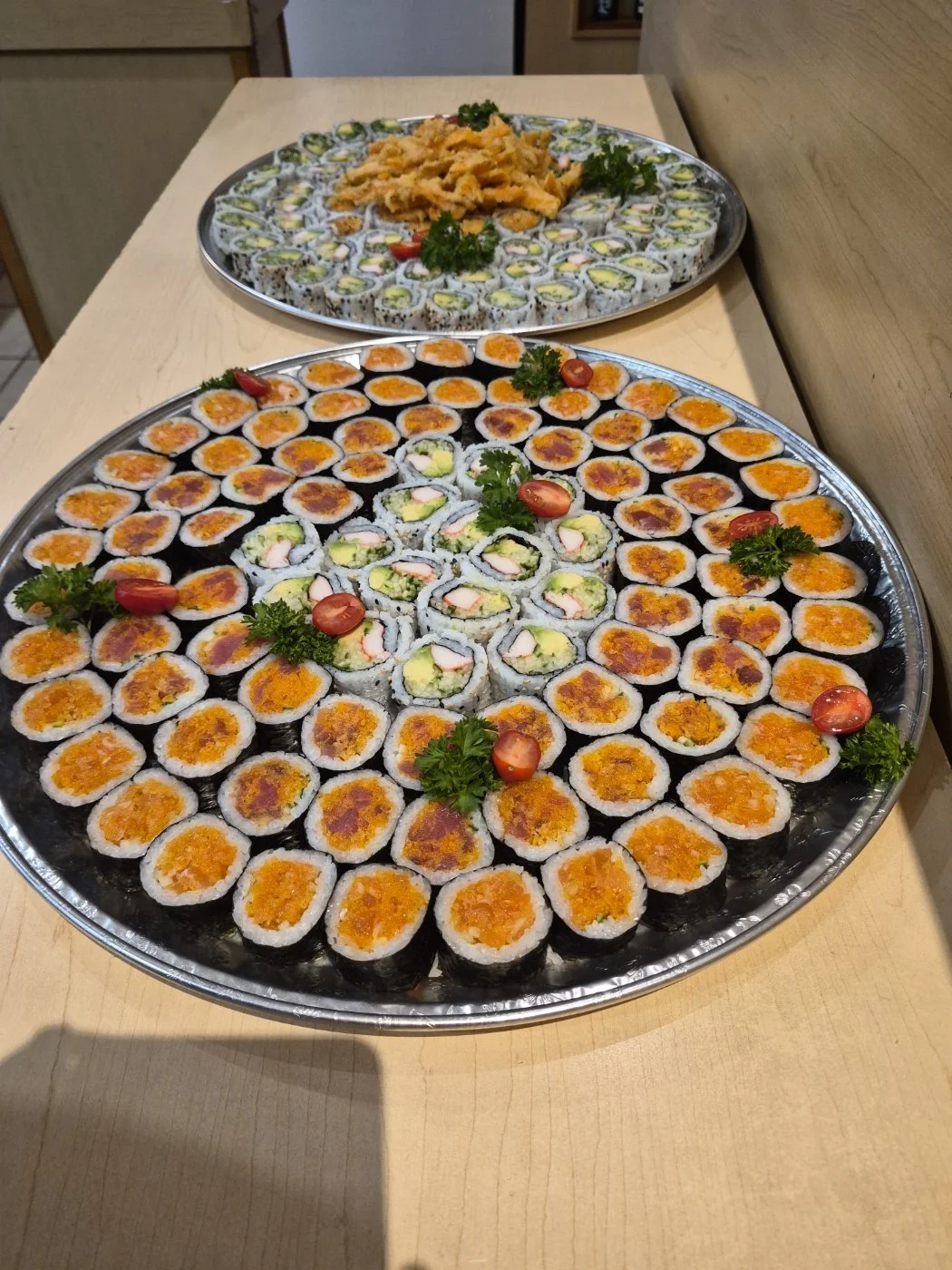 Large tray of assorted sushi rolls garnished with cherry tomatoes and parsley on a wooden table.