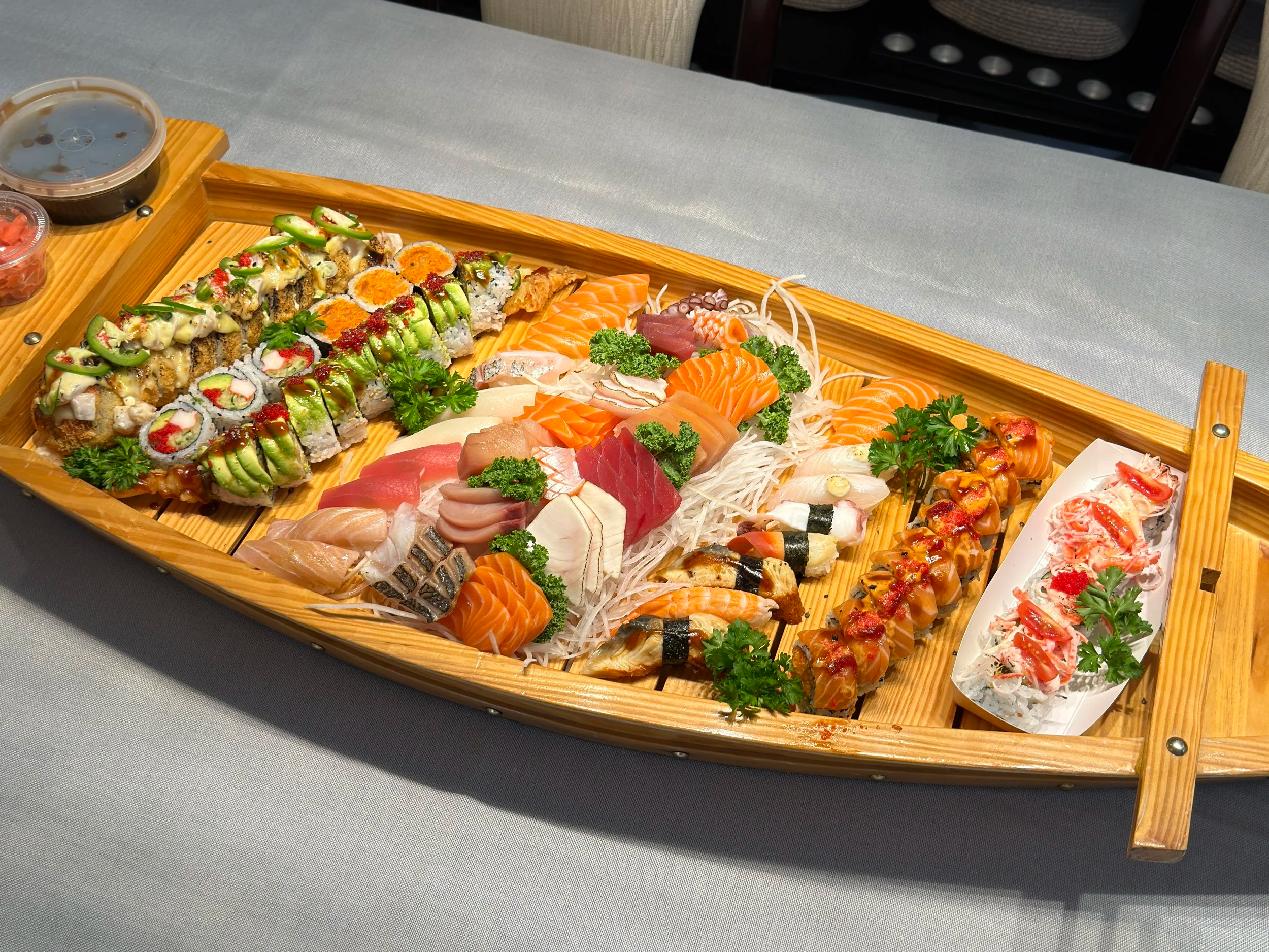 A wooden boat-shaped platter filled with assorted sushi and sashimi. Sushi boat.