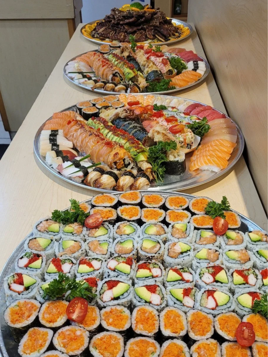 Assorted sushi platter with various rolls, sashimi, and garnishes on silver trays. Catering for a family gathering.