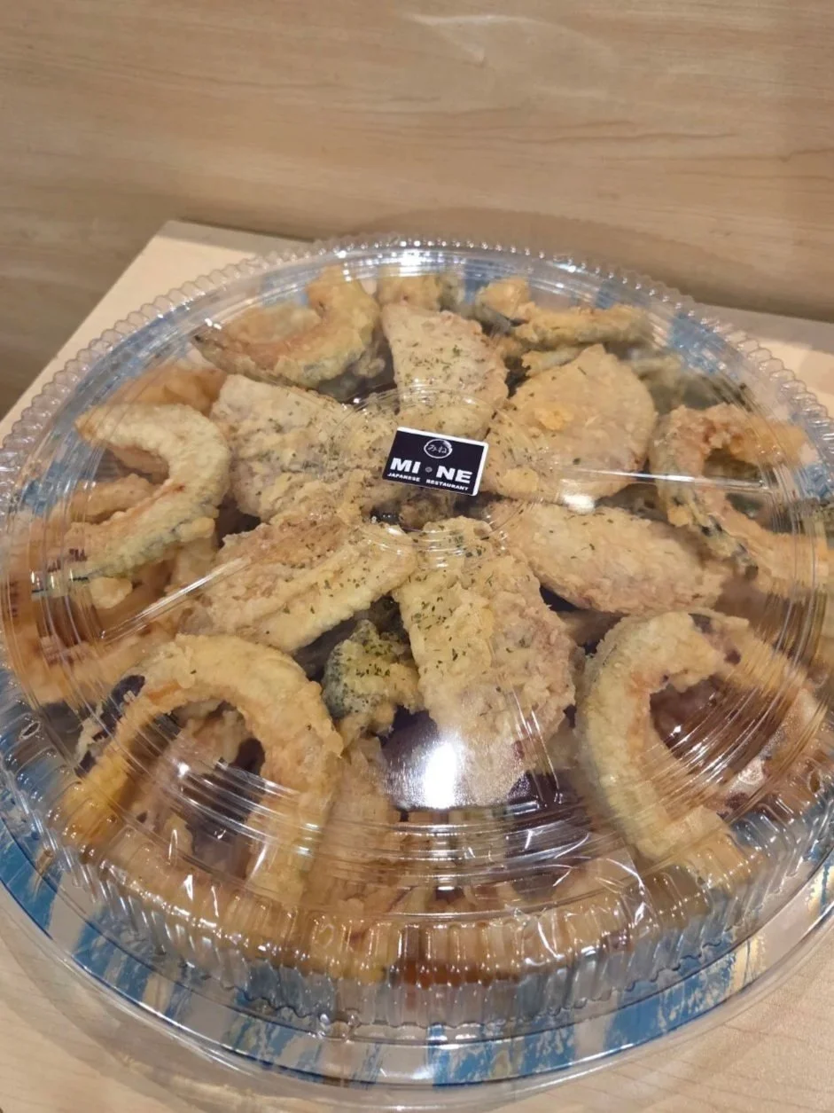 A clear plastic container of assorted Japanese tempura on a wooden surface.