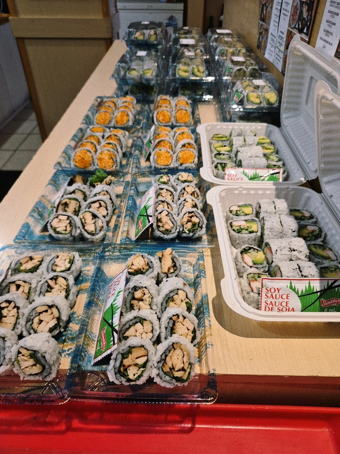 A display of various sushi rolls arranged on trays and plastic containers in a store or restaurant setting.