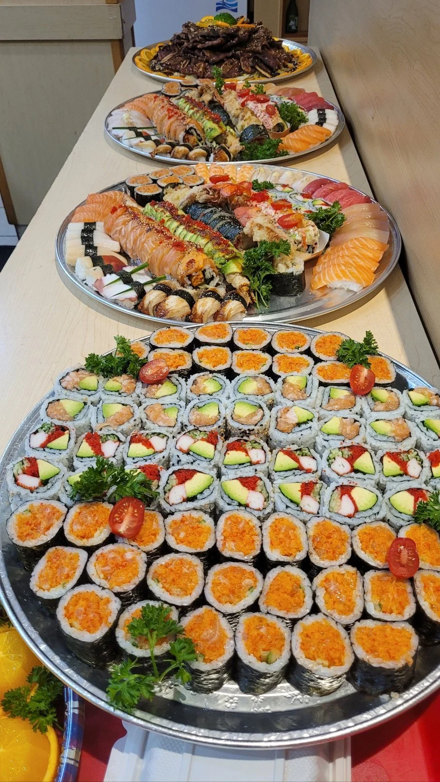 A long table with a variety of sushi platters, including assorted sushi rolls. Corporate event lunch catering, takeout.