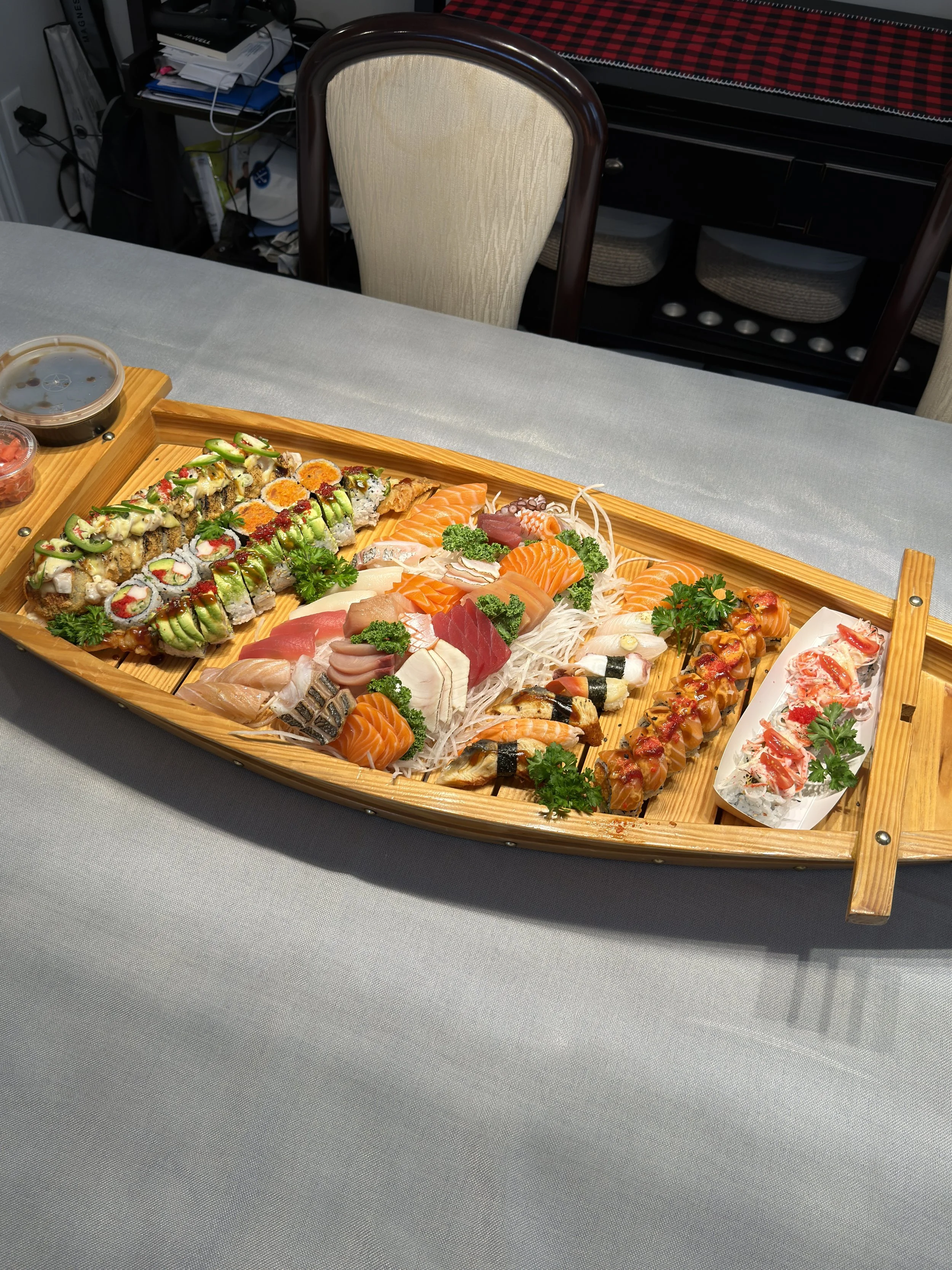 A large wooden boat-shaped platter of assorted sushi and sashimi on a white tablecloth. Sushi boat holiday party catering.