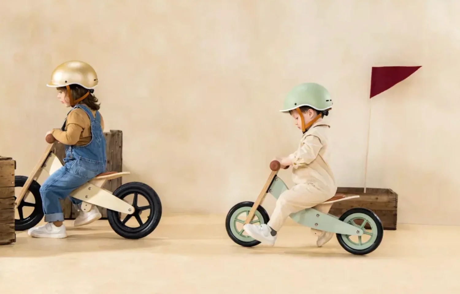 Two children riding small balance bikes indoors, wearing helmets.