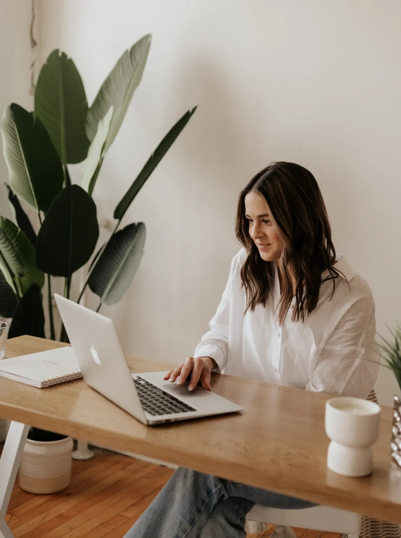 Kate Shewaga sitting at a wooden desk working on a silver MacBook laptop.