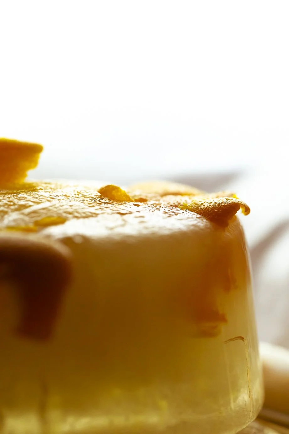 Close-up of a lemon tart with a glossy lemon glaze, showing the textured surface and a lemon peel decoration on top.