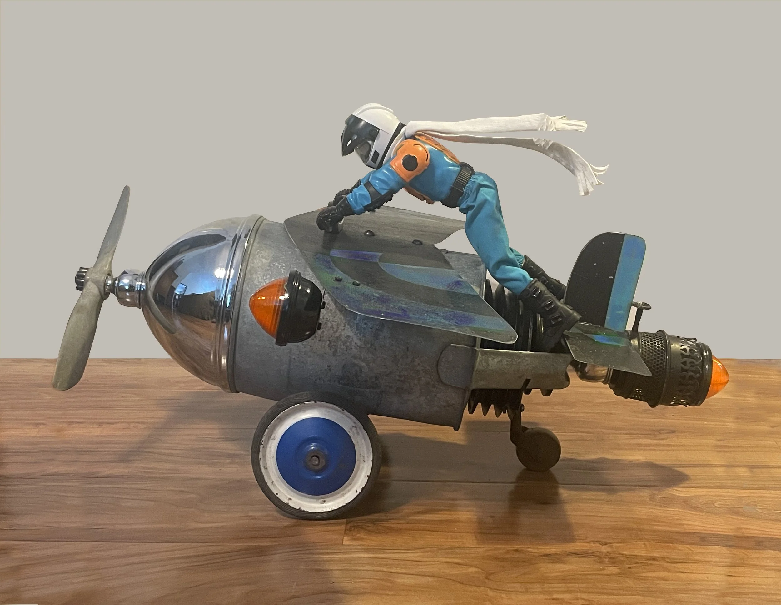 Fearless Flyer 71, 2026 /
propeller, motorcycle lights,
cart wheels, watering can, caster, action figure, fabric, wire, reclaimed metal sign /
28 x 24 inches