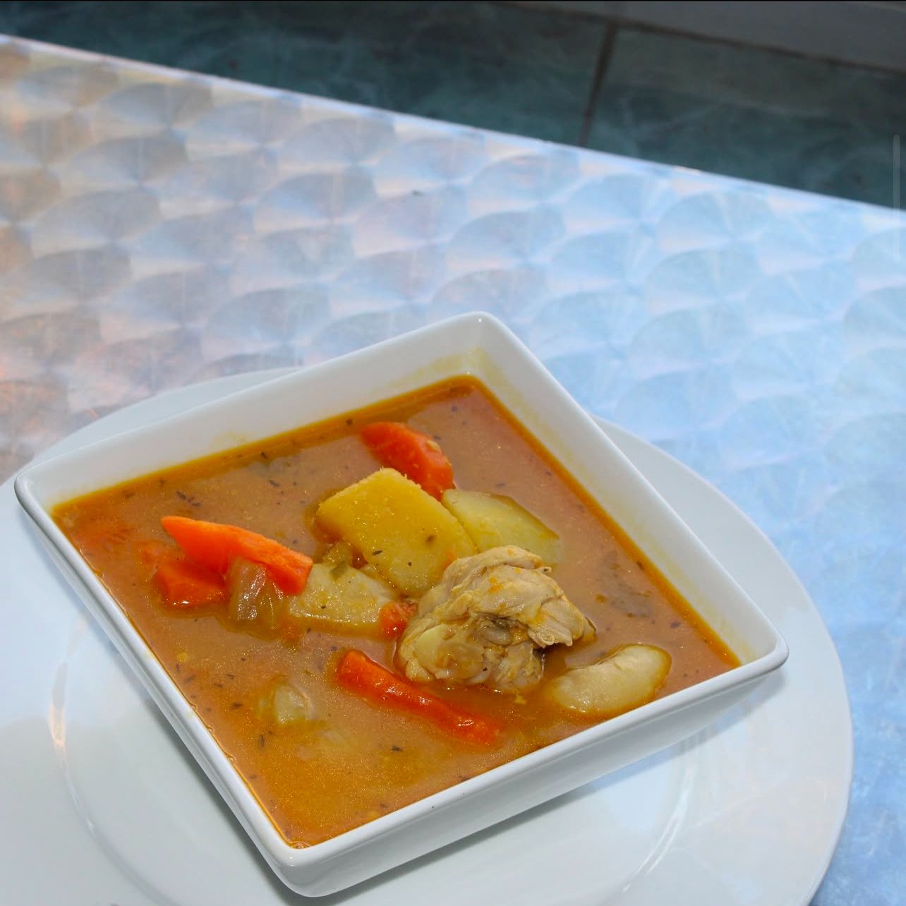 Bowl of soup with chicken, carrots, and potatoes on a table