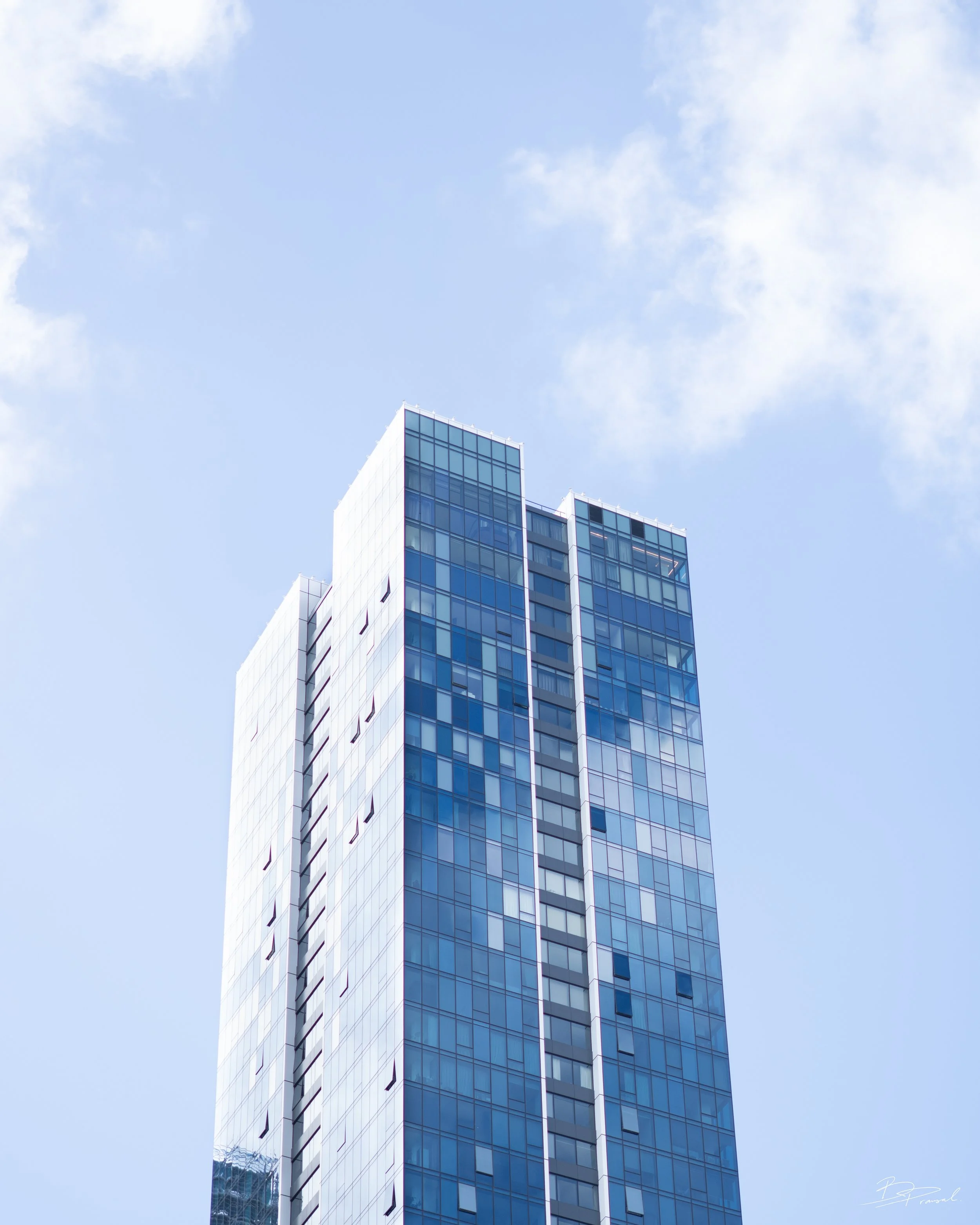 Tall modern glass skyscraper against a blue sky with a few clouds.