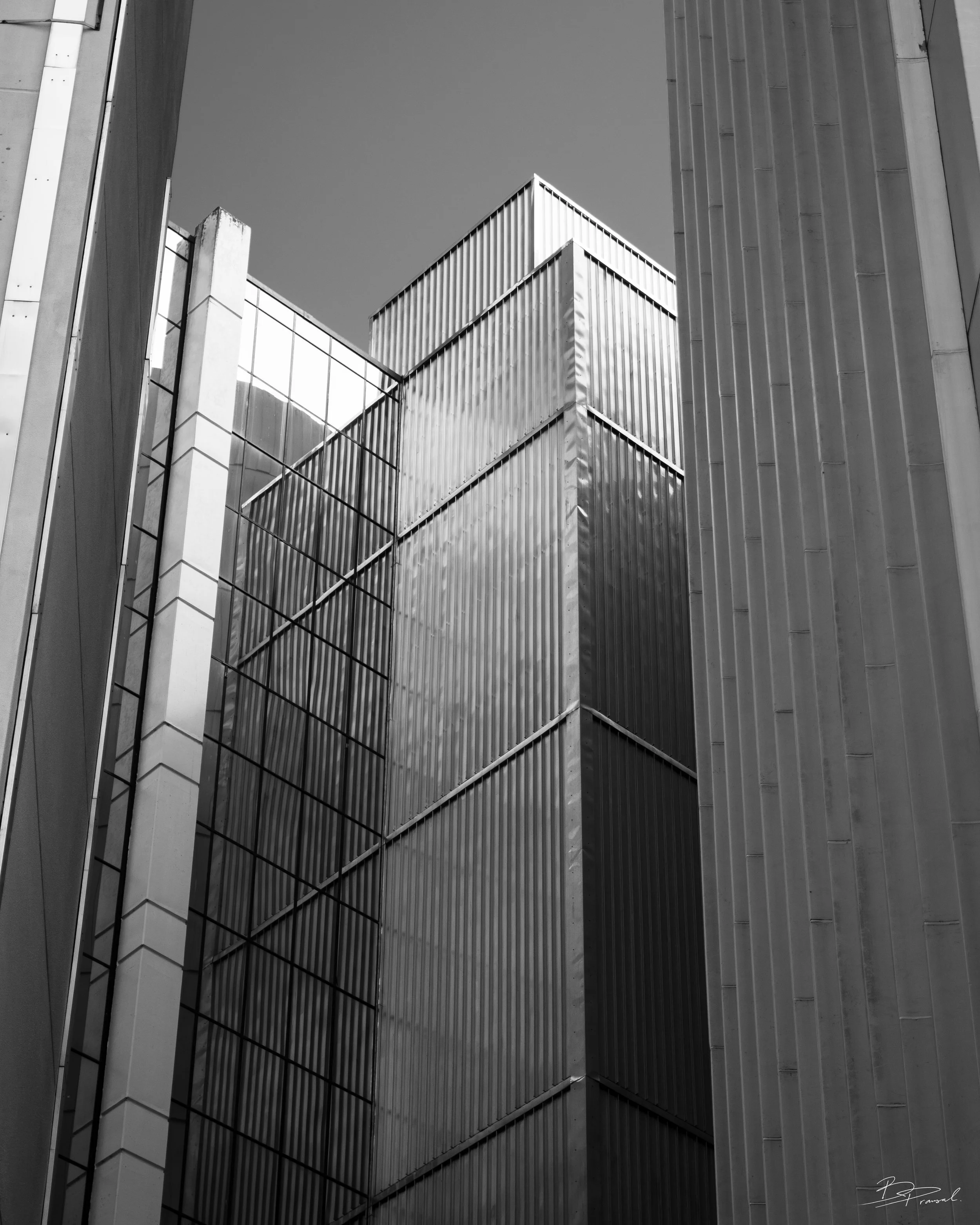Black and white photo of modern architectural buildings with various textured panels and glass windows, viewed from a low angle.