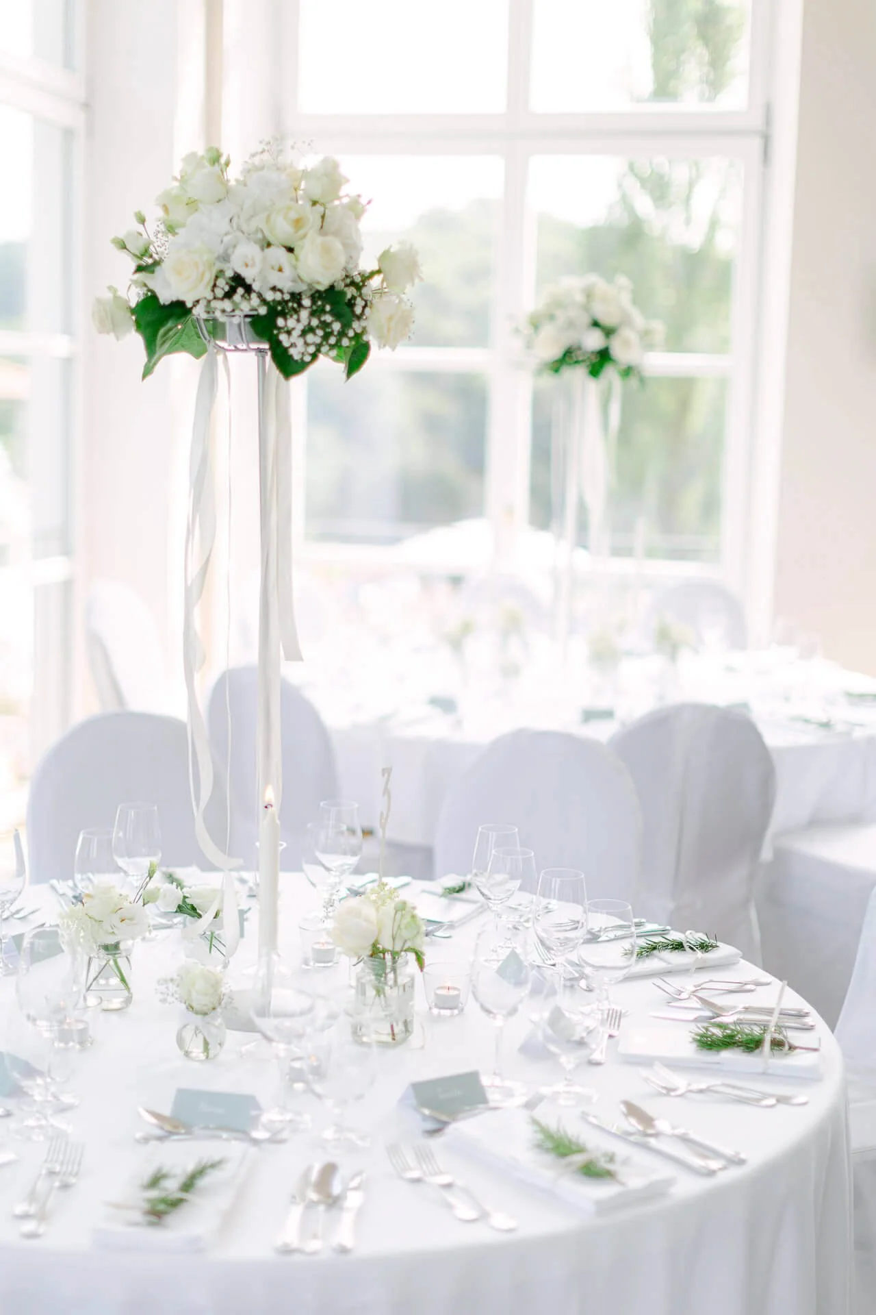 Elegant gedeckter Hochzeitstisch mit weißer Tischdecke, Blumenarrangement und Kerzen.